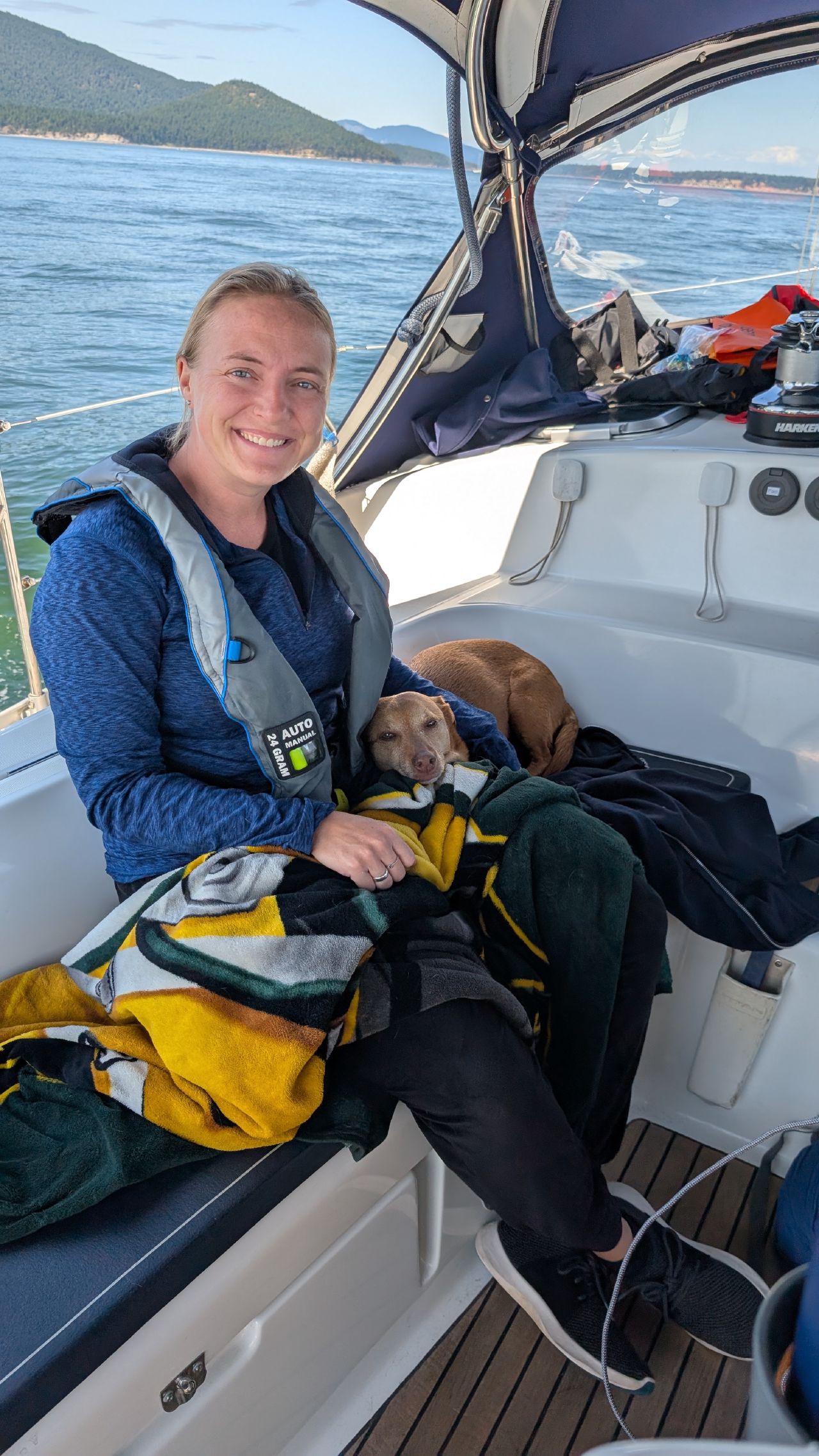 Rachel sitting in the cockpit with Maui the dog wrapped in a blanket in the San Juan Islands