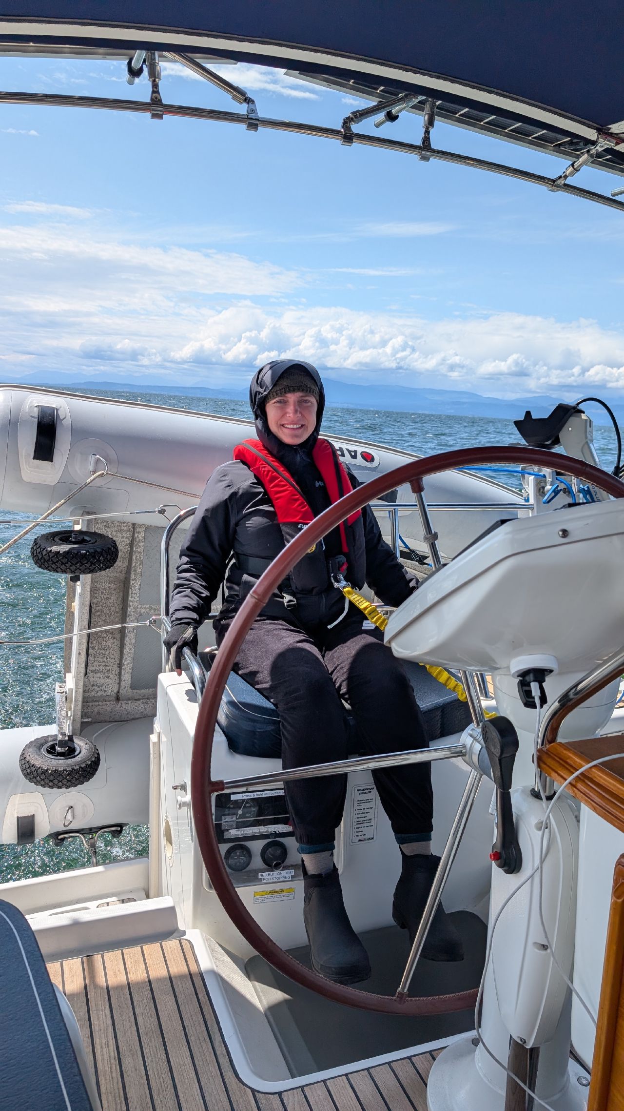 Rachel smiling at the helm in foul weather gear and life jacket crossing the Strait of Georgia