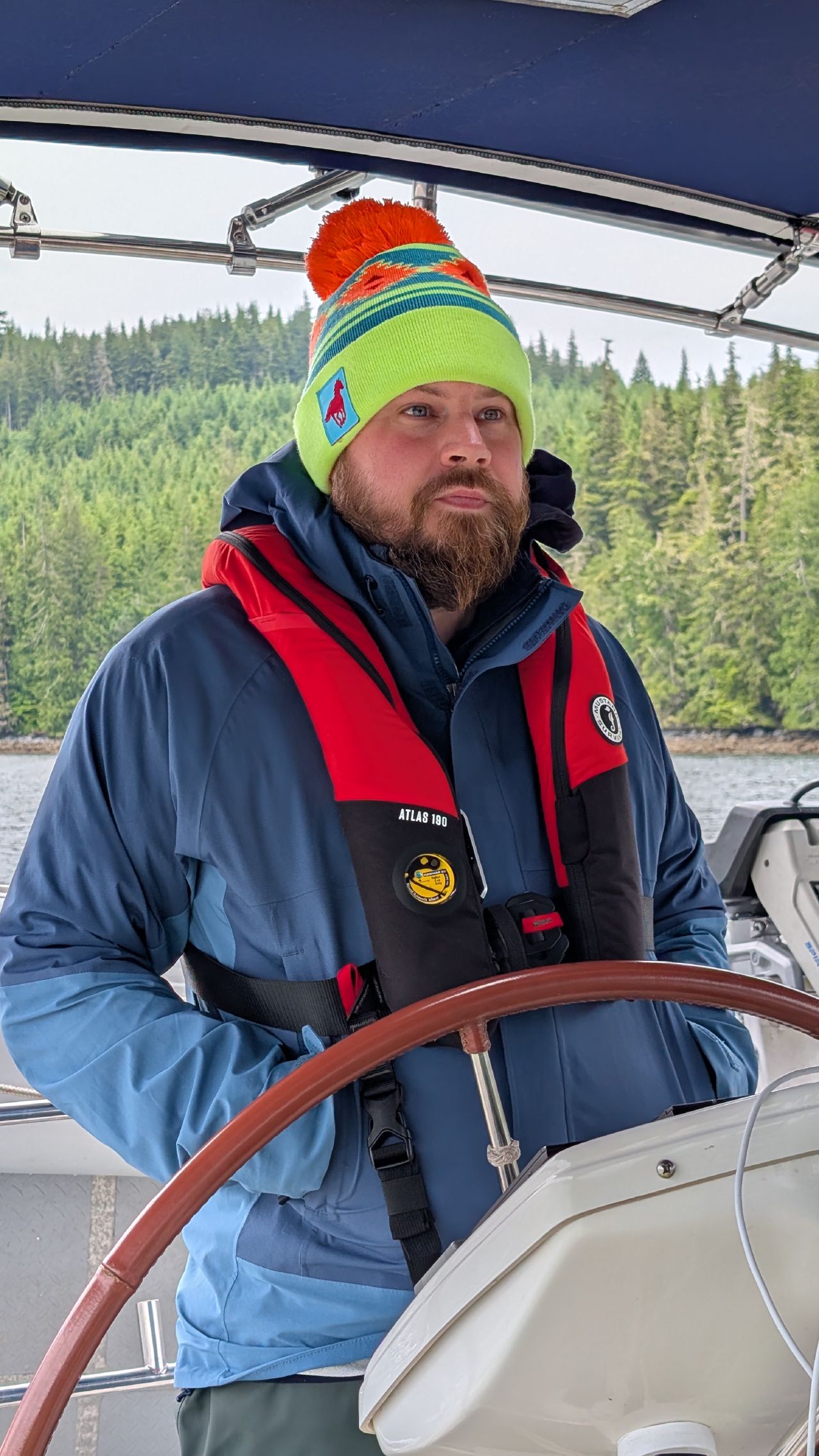 Brian focused at the helm in a colorful beanie and life jacket navigating Johnstone Strait