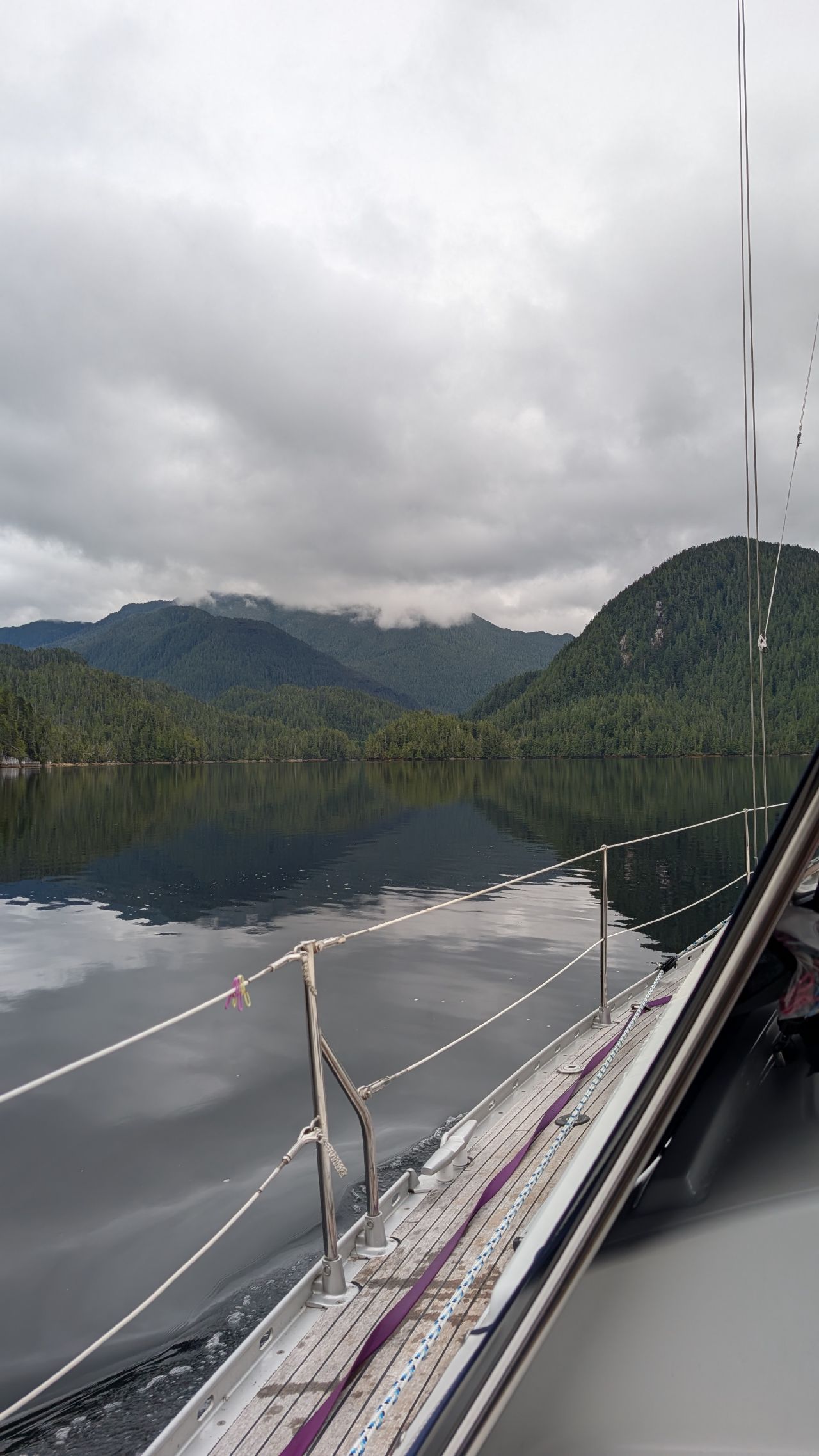 Glass-calm water reflecting mountains viewed from the bow of SV Yahara at Oyster Bay