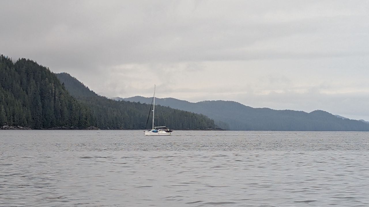 A lone sailboat anchored with misty forested mountains in the background