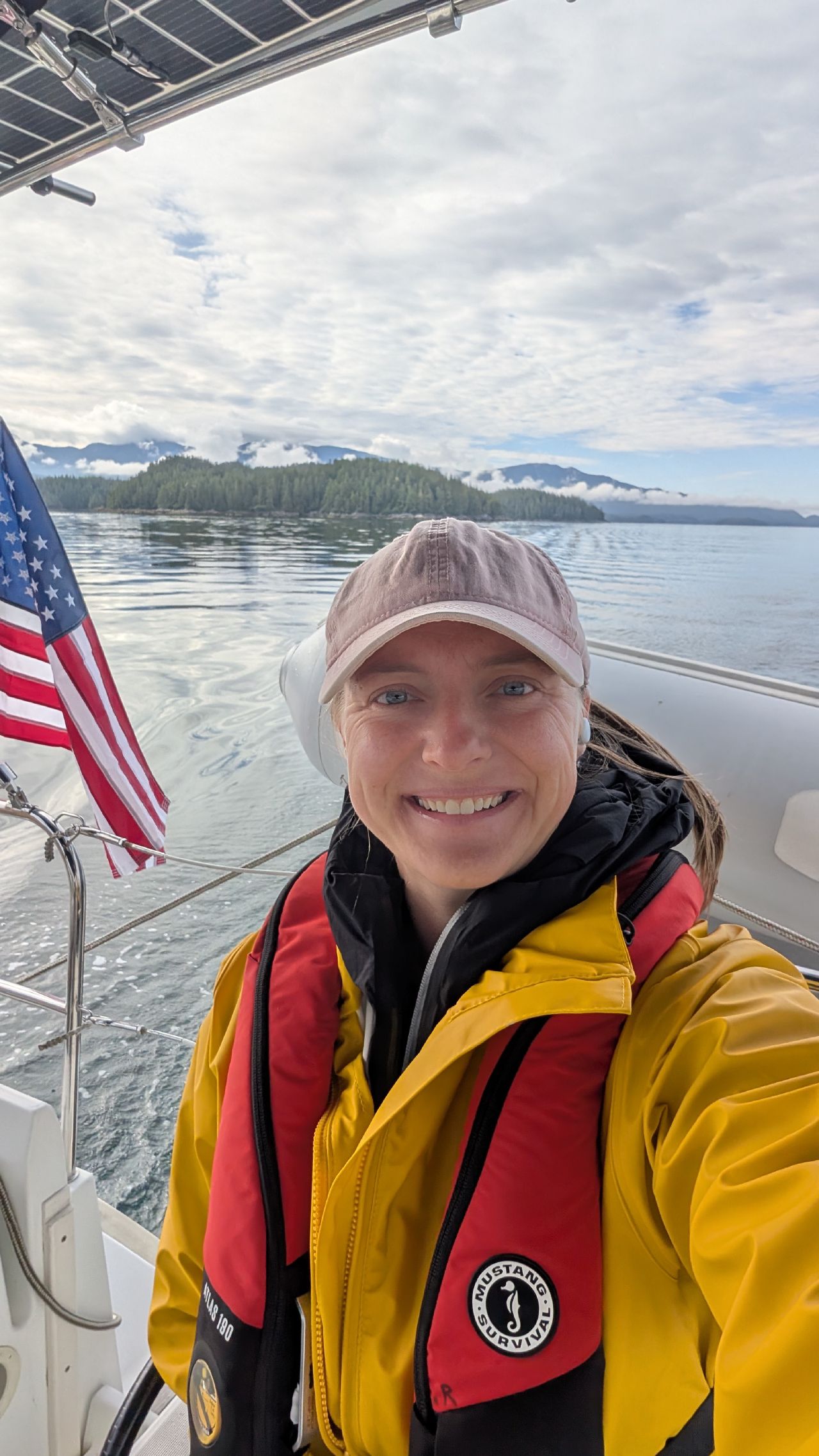 Rachel smiling in her life jacket and foul weather gear at the helm on the passage to Codville