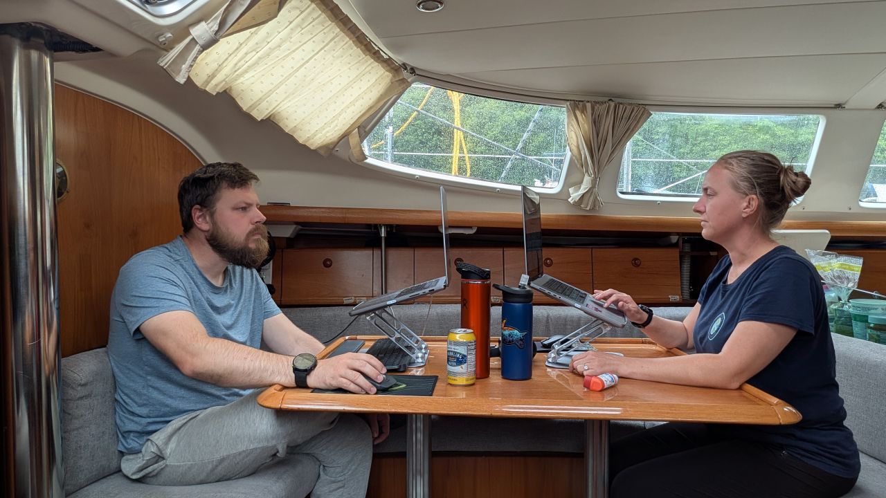 Brian and Rachel working on laptops at the salon table below deck on a rainy day