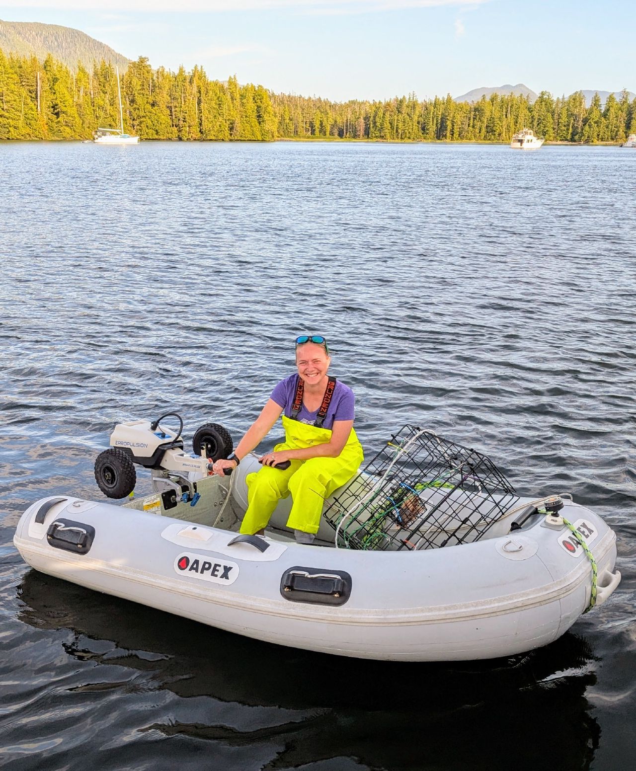 Rachel in yellow rain bibs sitting in the dinghy with the crab trap at Rescue Bay