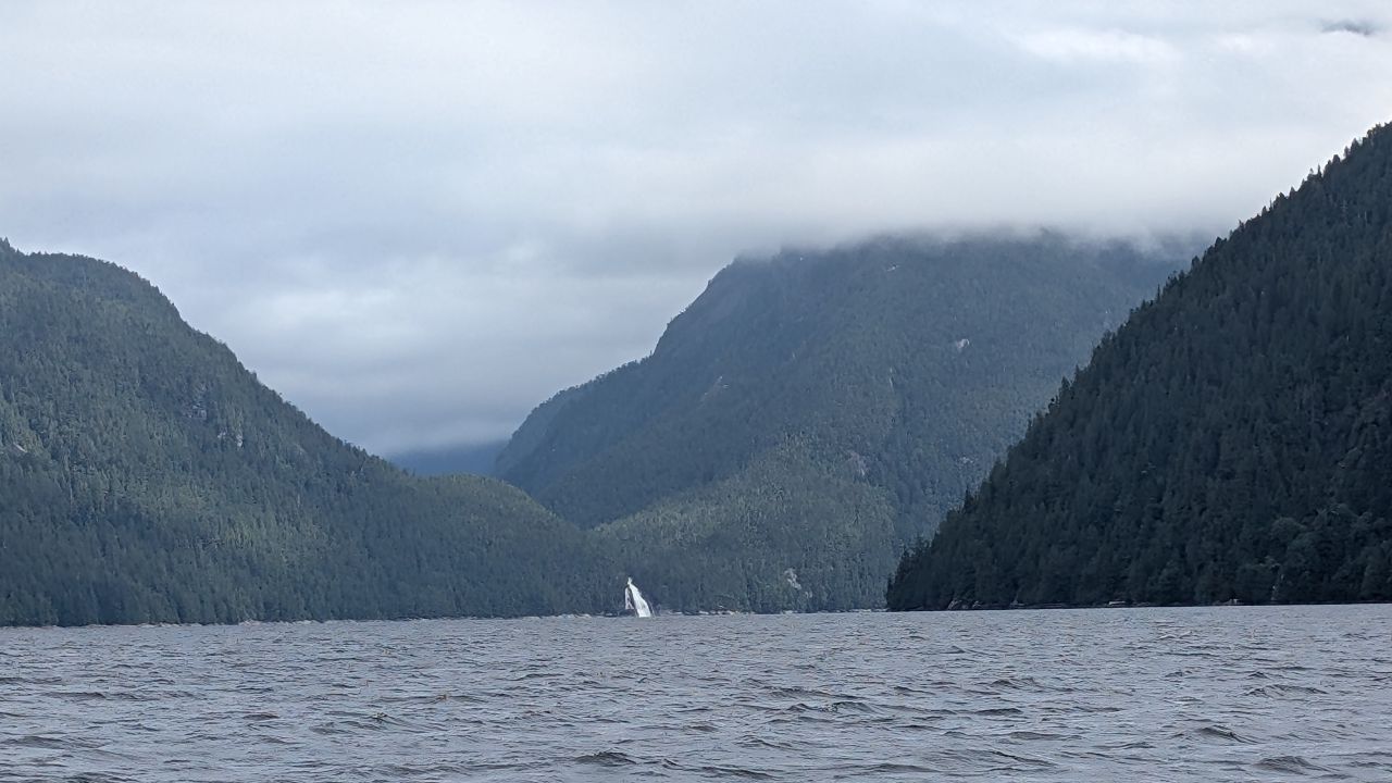 Cloud-covered mountains flanking the channel with a waterfall visible between the peaks
