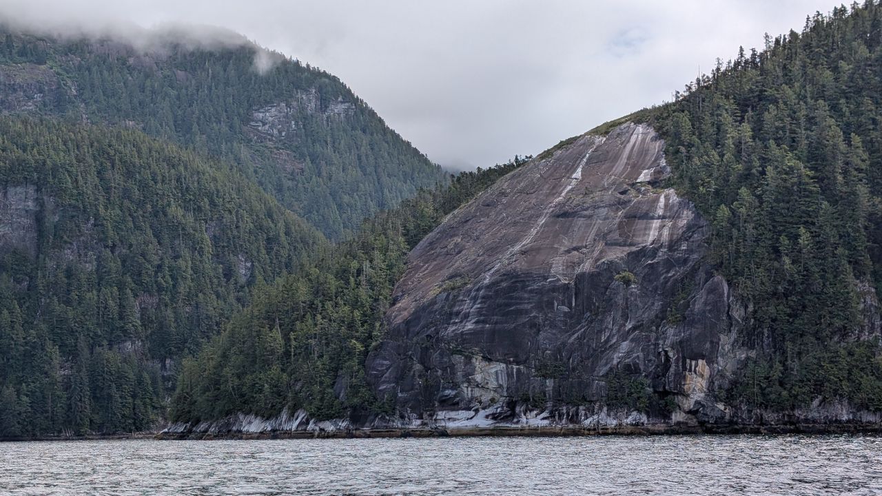 Dramatic exposed granite cliff face rising from the water in Mathison Channel with clouds overhead