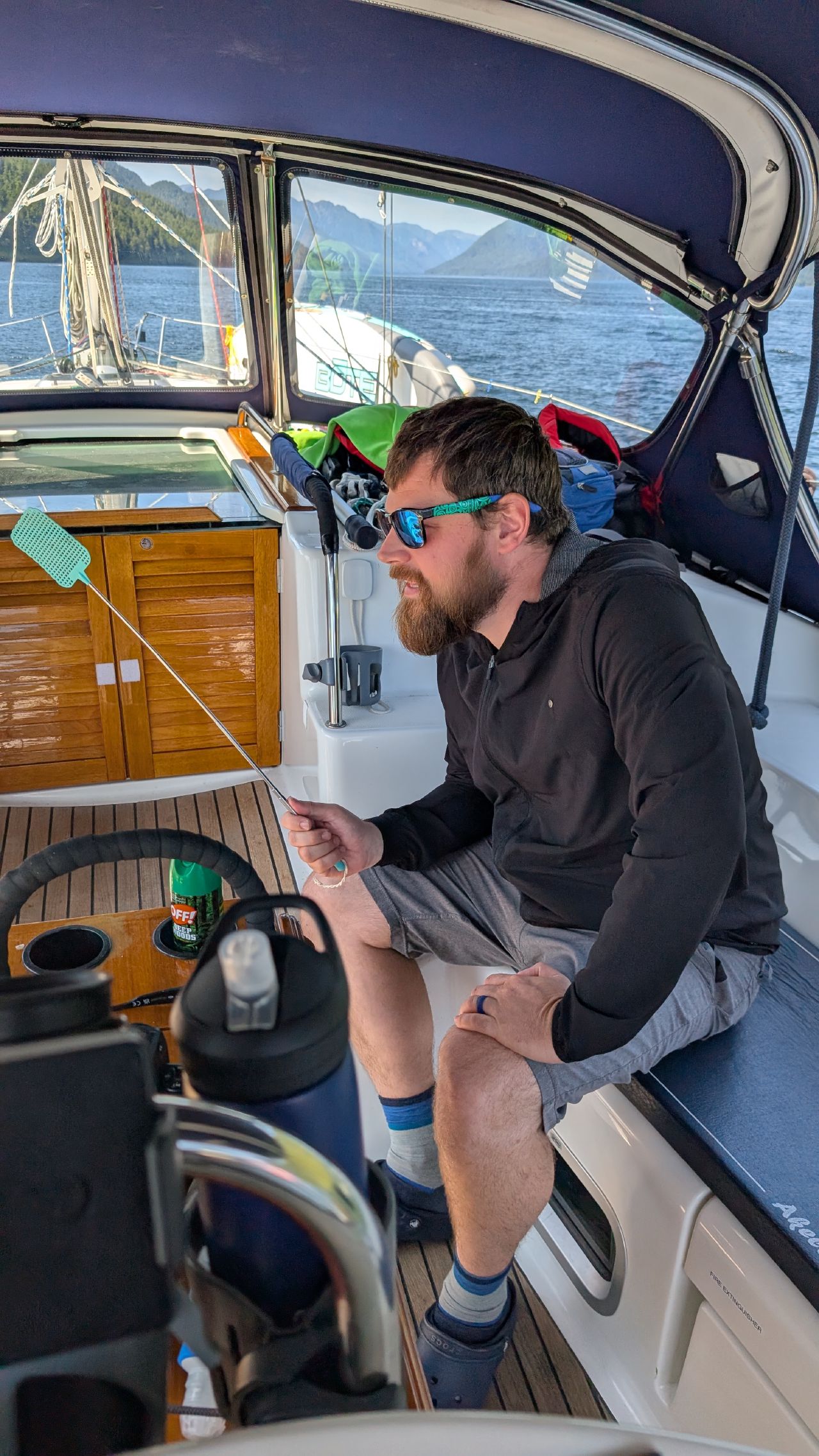 Brian sitting in the cockpit holding a fly swatter, battling the relentless deer flies at Khuntz Bay