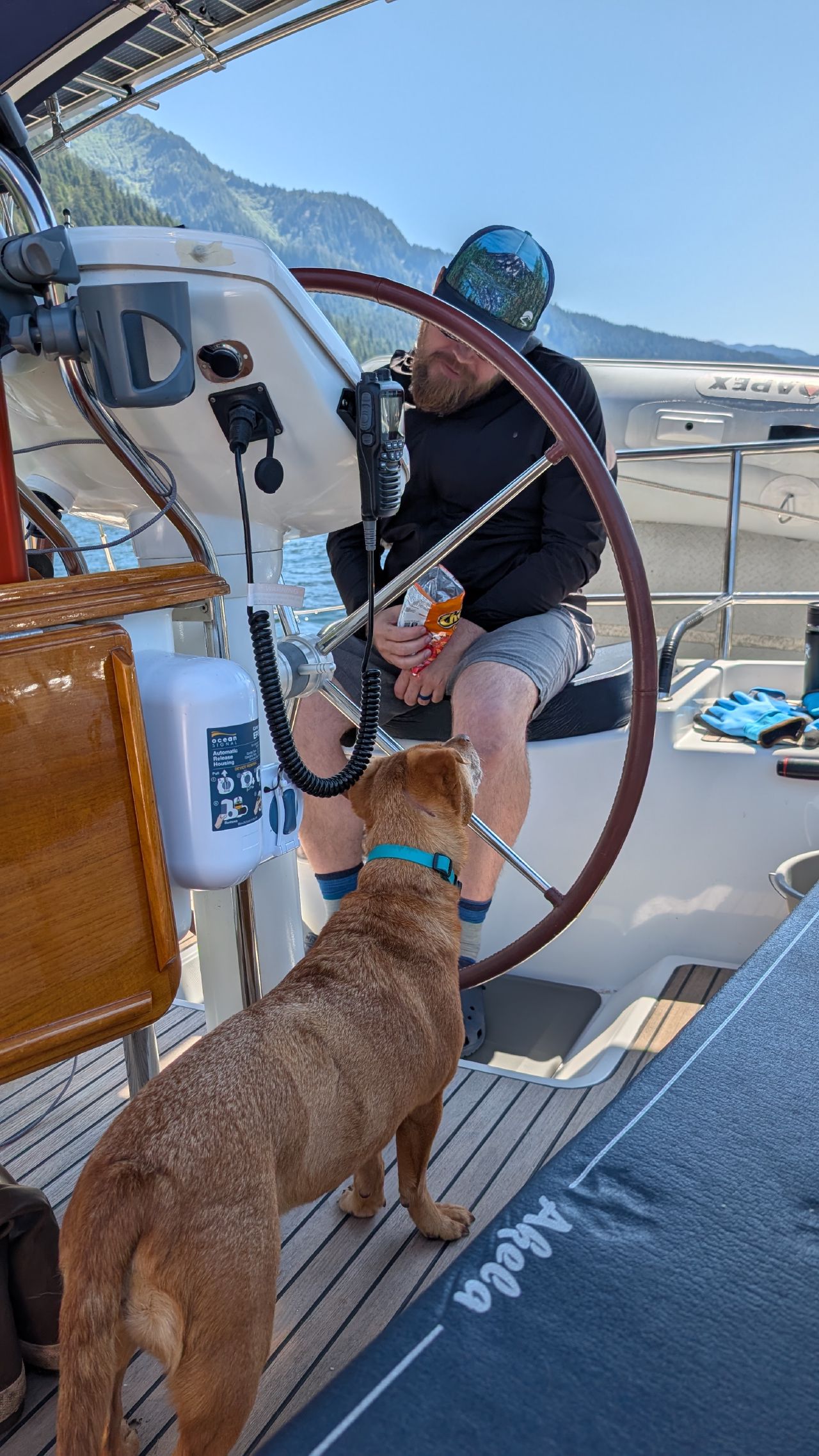 Brian eating Cheetos at the helm while Maui watches hopefully from below