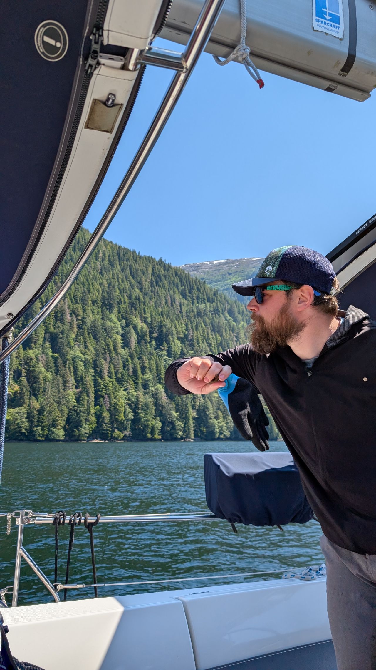 Brian using a fishing glove to swat deer flies in the cockpit with forested mountains behind
