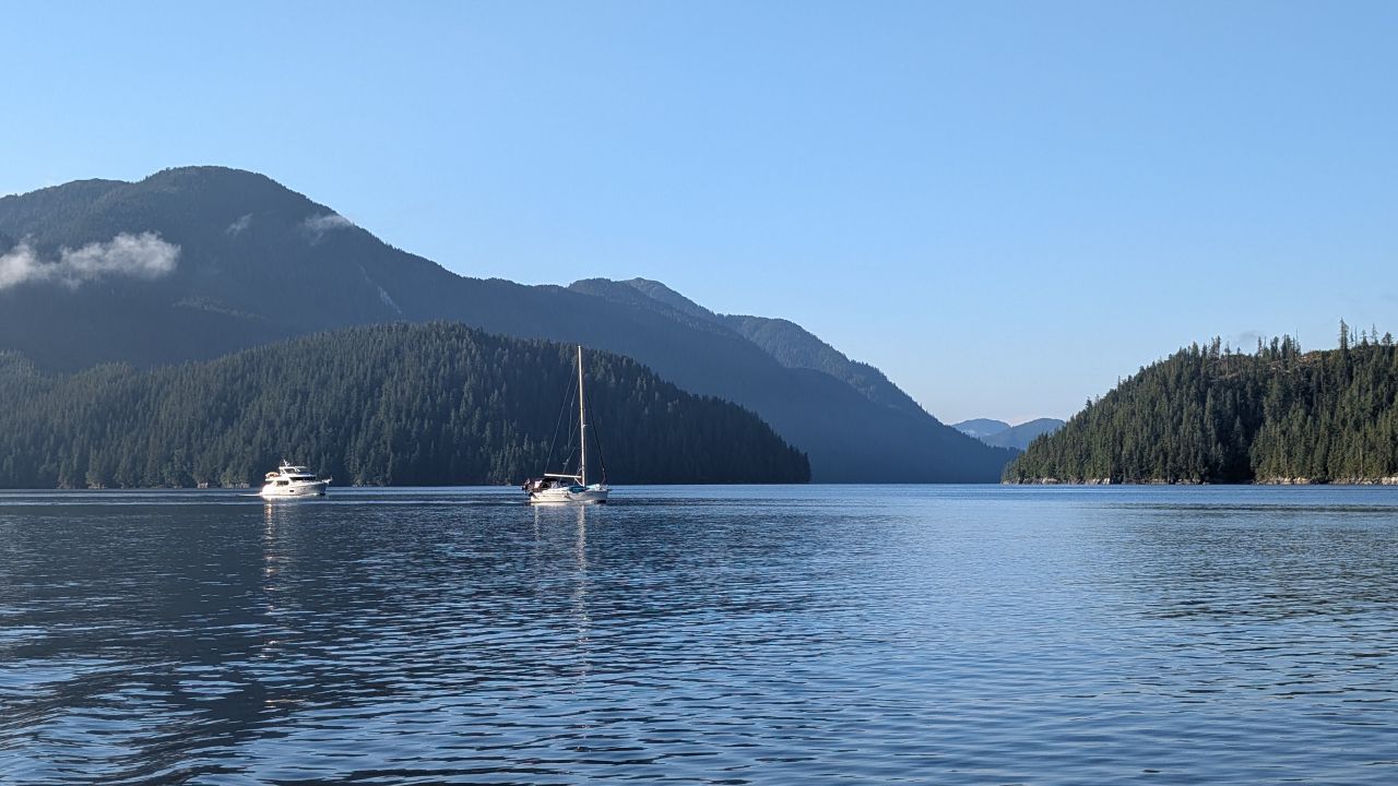 Sailboat and powerboat anchored in calm waters with mountains in the background