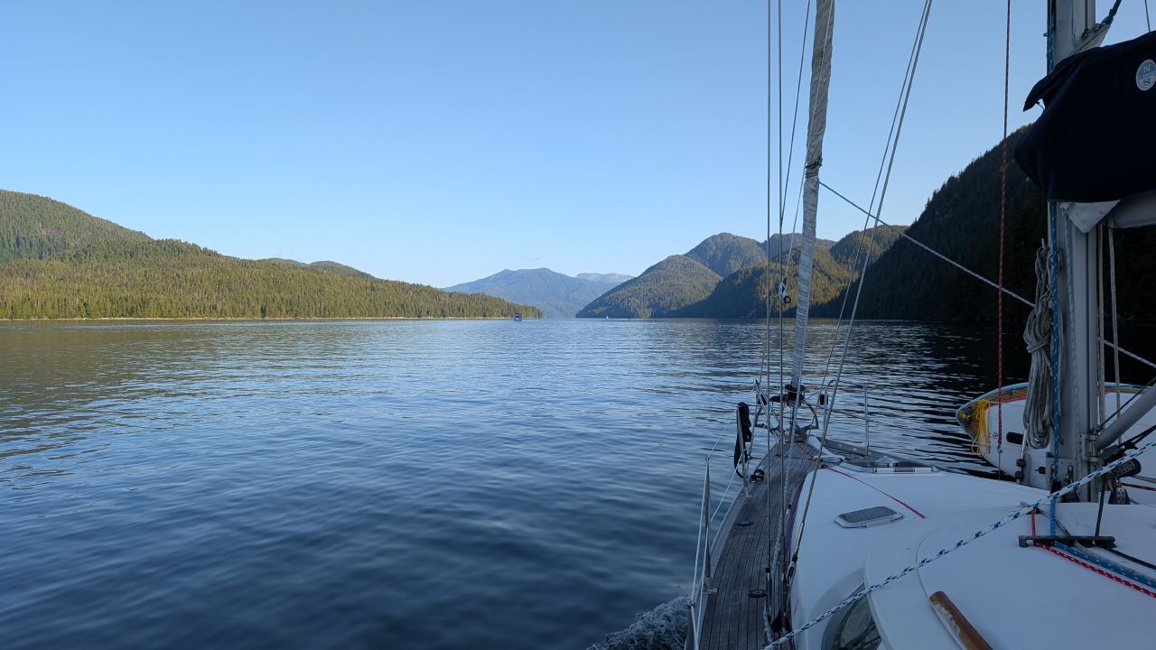 View from the deck of SV Yahara motoring through a glassy channel flanked by forested mountains