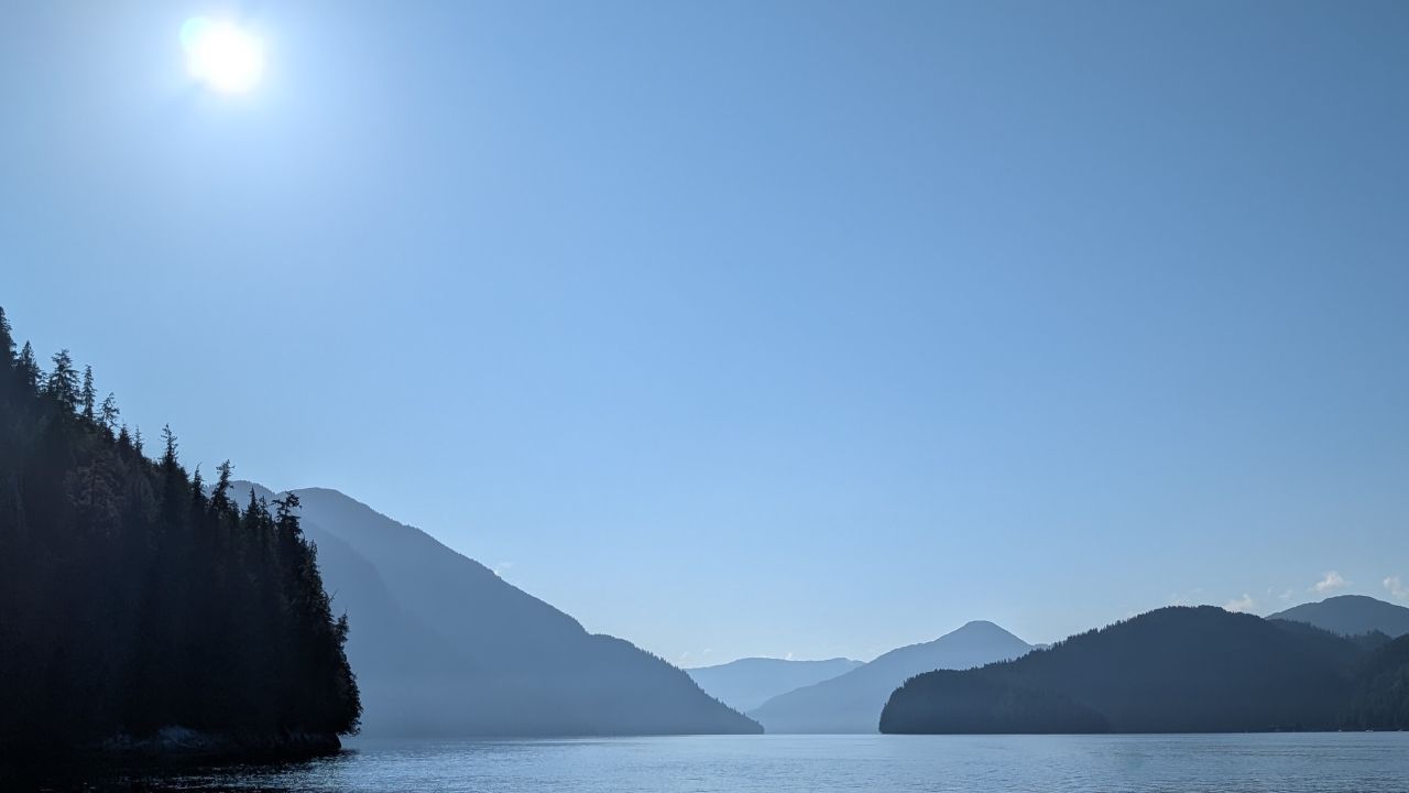 Hazy layered mountain silhouettes with the sun beaming overhead on the passage to Swanson Bay