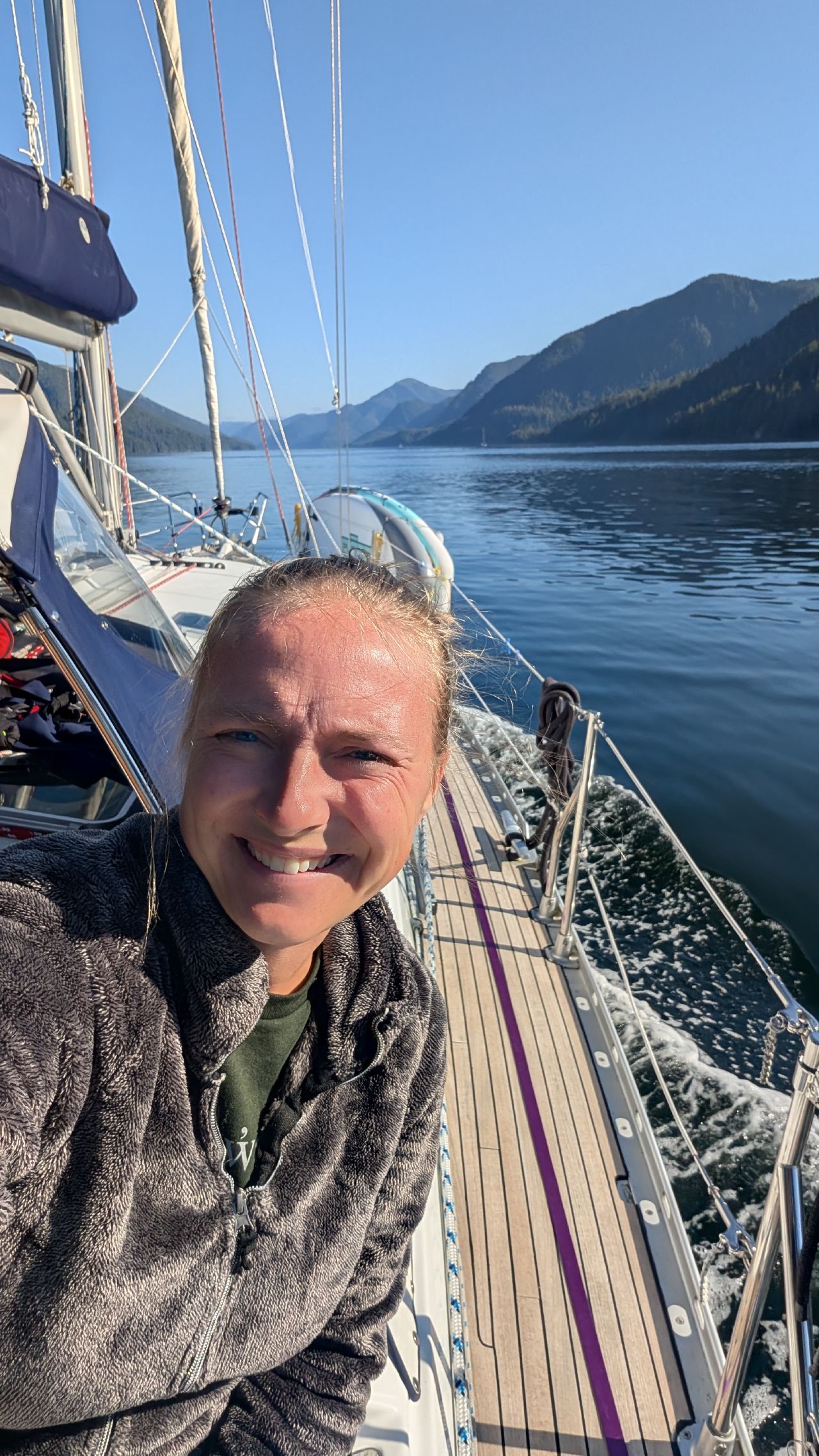 Rachel smiling for a selfie on deck with mountains and calm water behind on the passage to Swanson Bay