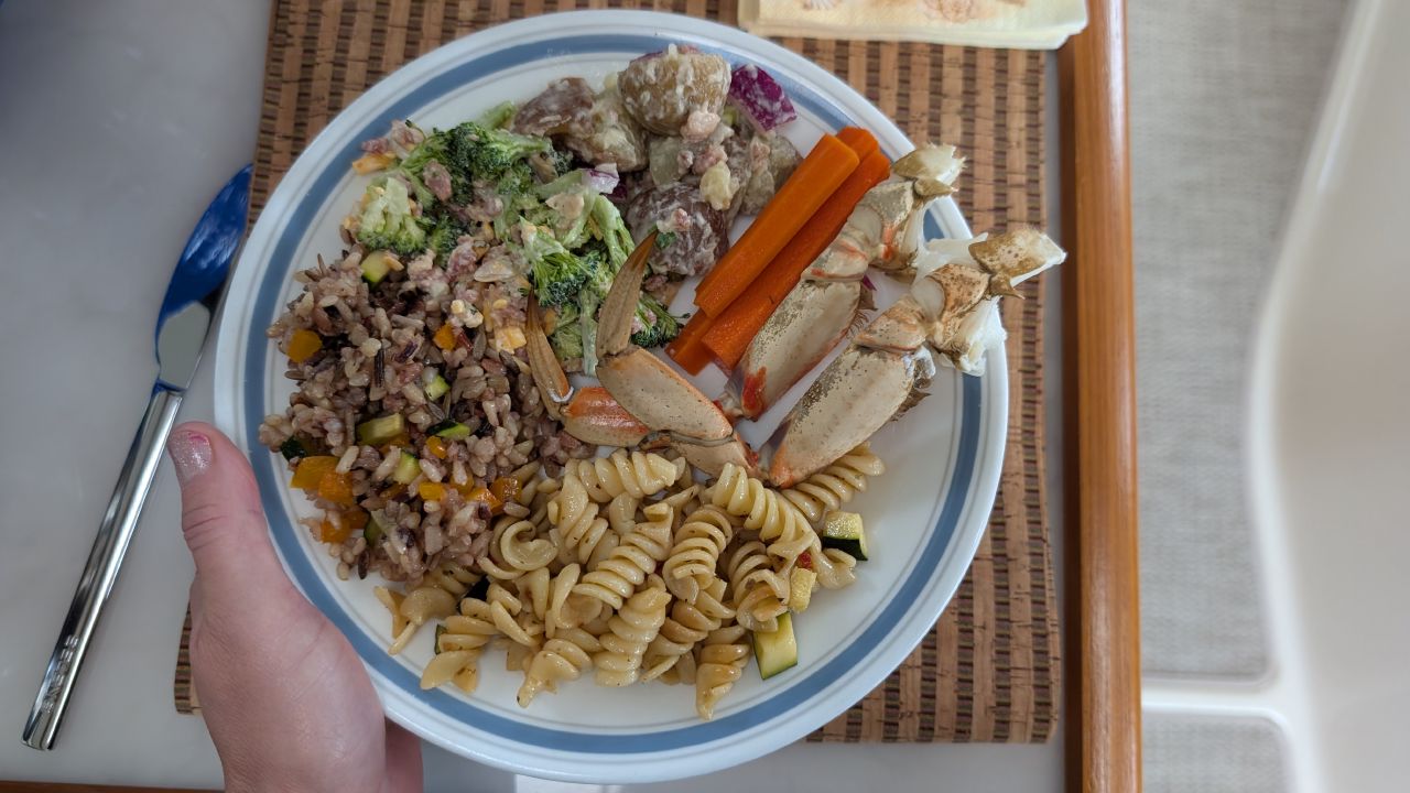 Potluck lunch plate loaded with crab legs, pasta salad, wild rice, broccoli salad, and potato salad