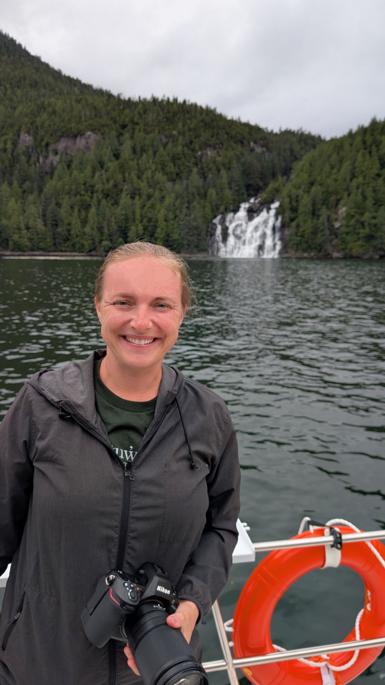 Rachel smiling with her camera and a life ring, the Poison Cove waterfall visible behind her
