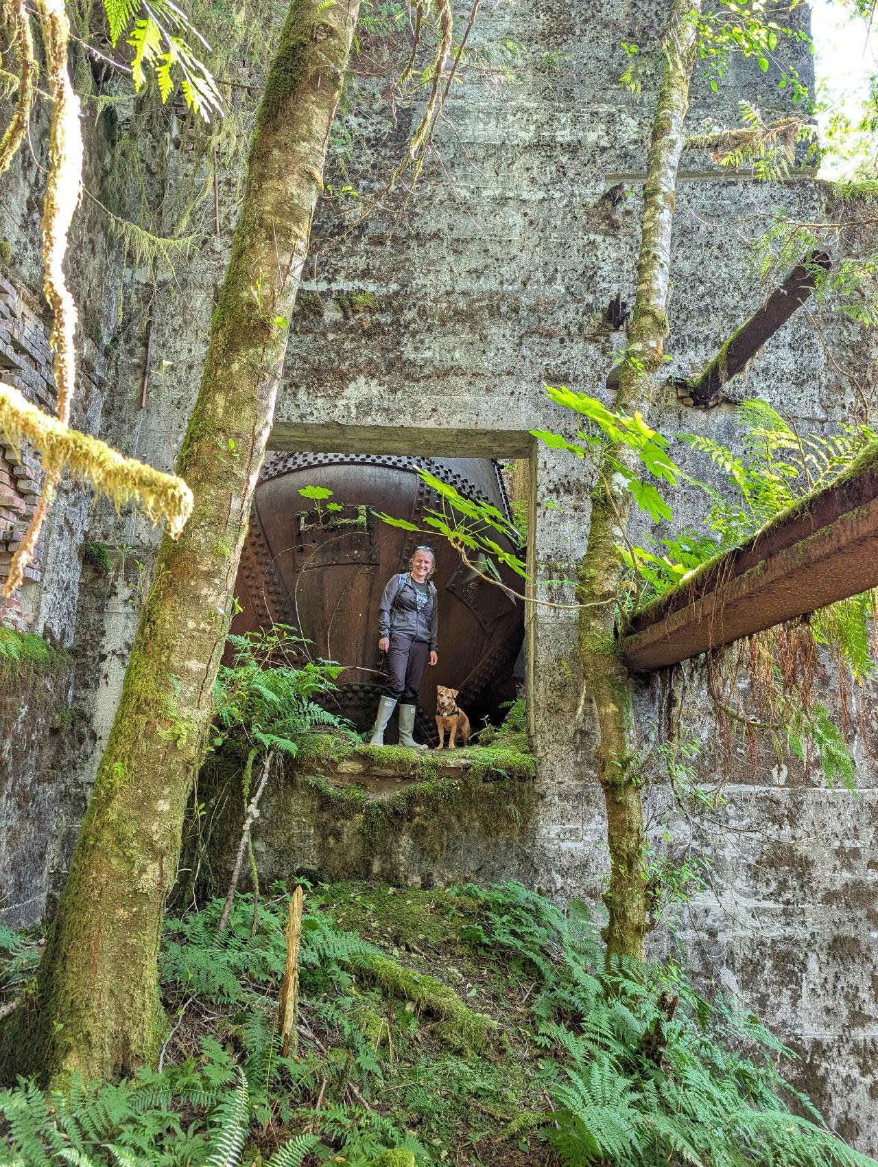 Rachel and Maui standing in a doorway of the overgrown concrete ruins with a large rusted boiler behind them
