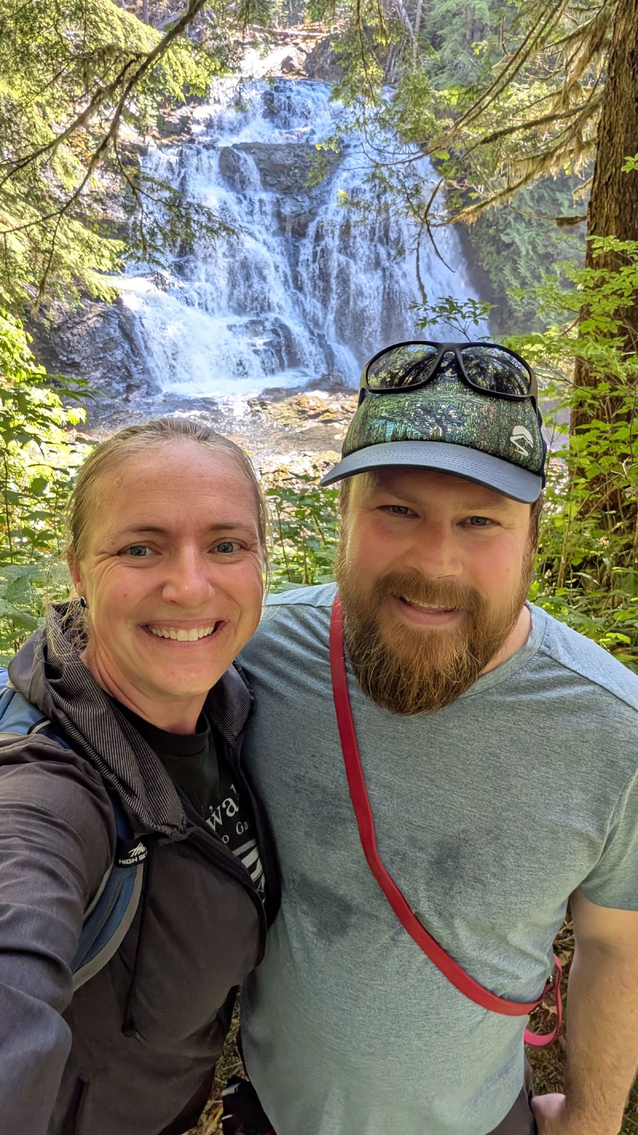 Rachel and Brian smiling for a selfie with a beautiful multi-tiered waterfall at Swanson Bay