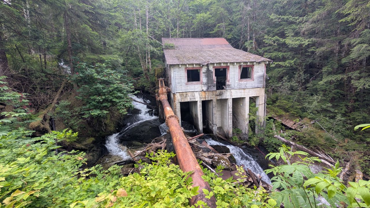 Abandoned concrete powerhouse building with a rusted pipe straddling a waterfall in the Butedale rainforest