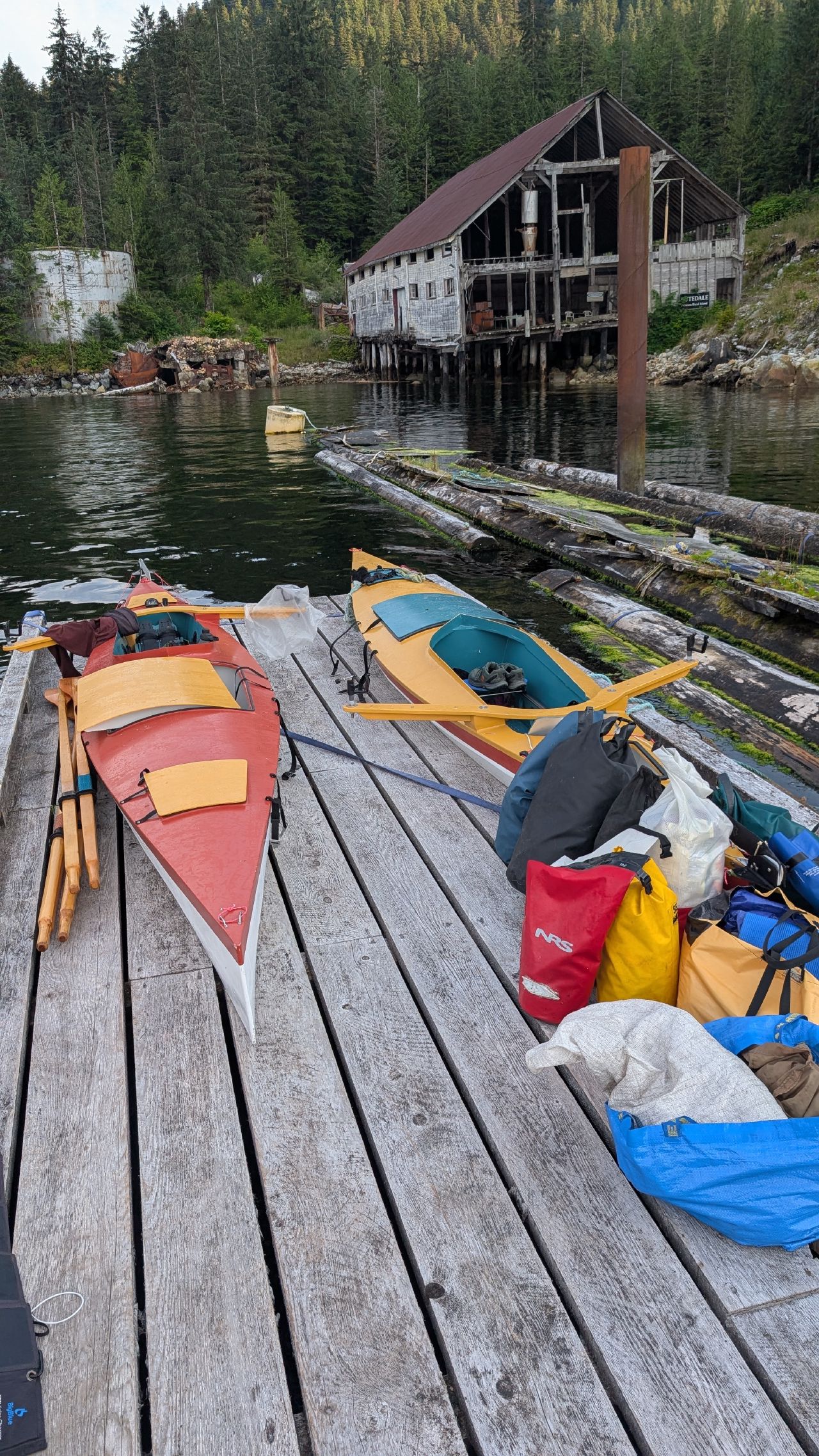 Colorful row boats and dry bags on the dock at Butedale with the old cannery building across the water
