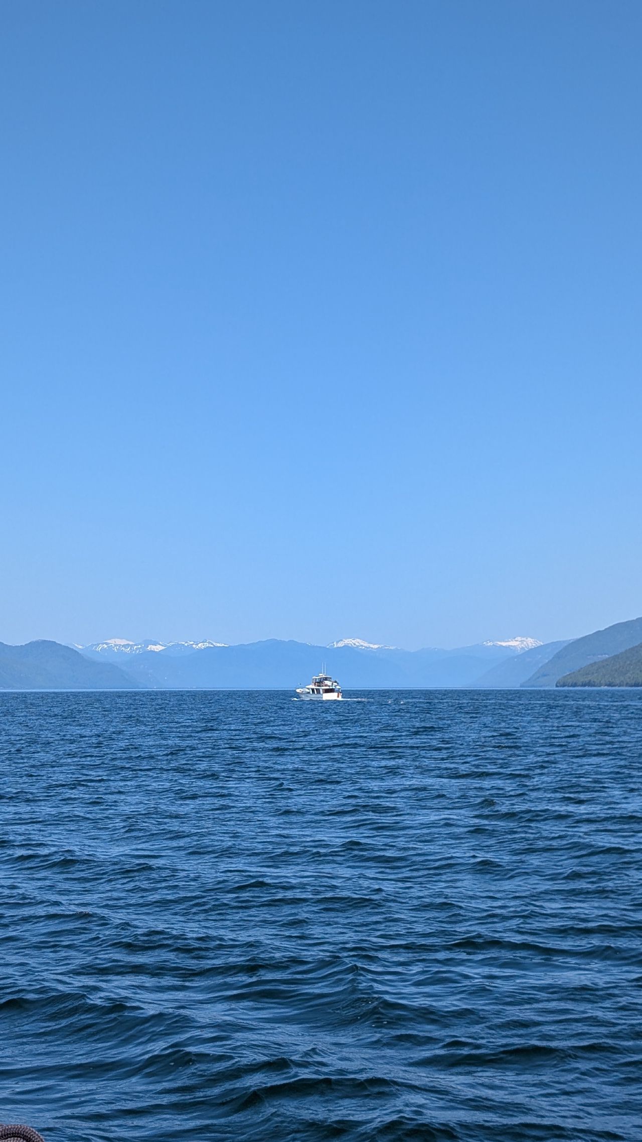Distant boat on open blue water with snow-capped mountains along the horizon