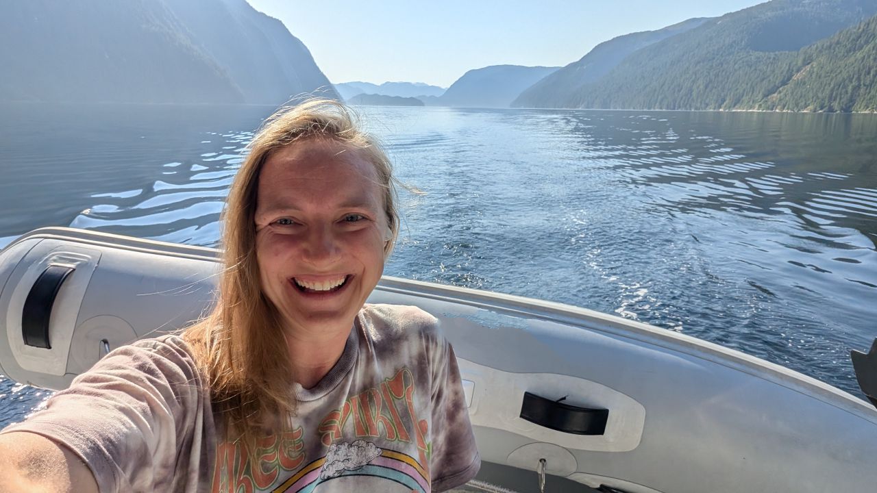 Rachel smiling in a selfie with mountains and calm water stretching behind her