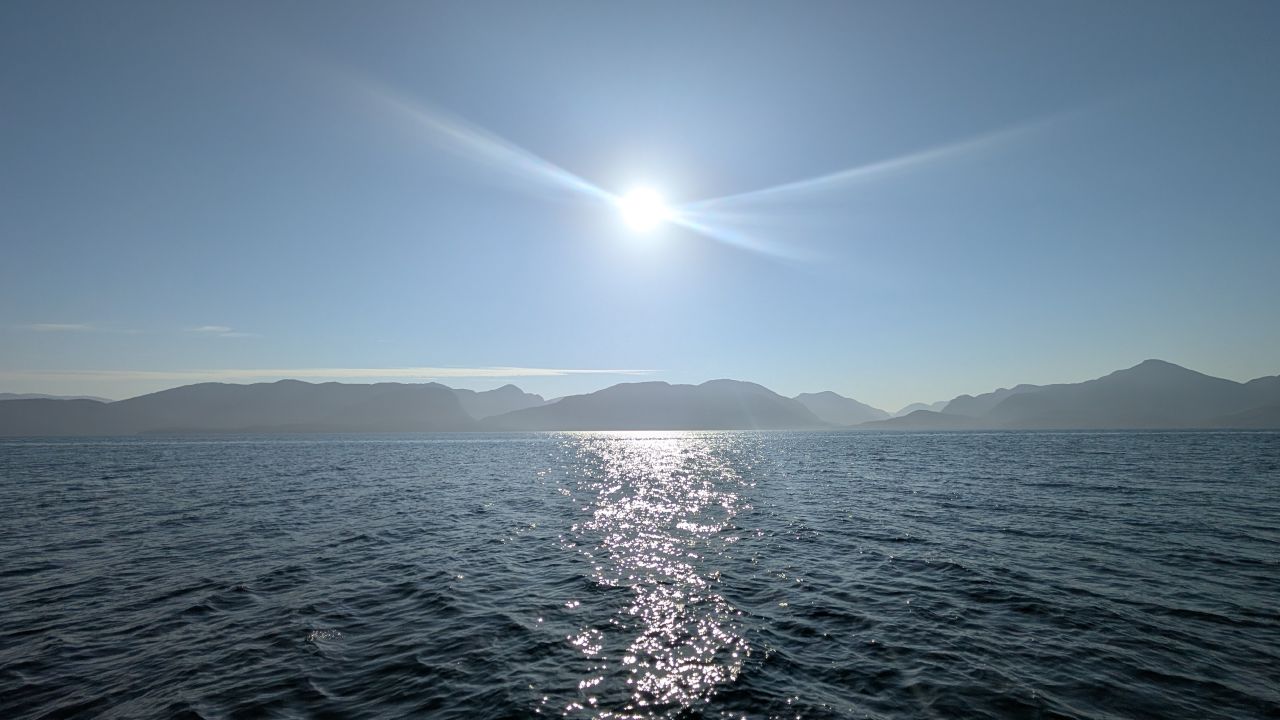 Sun sparkling on open water with mountain silhouettes on the horizon