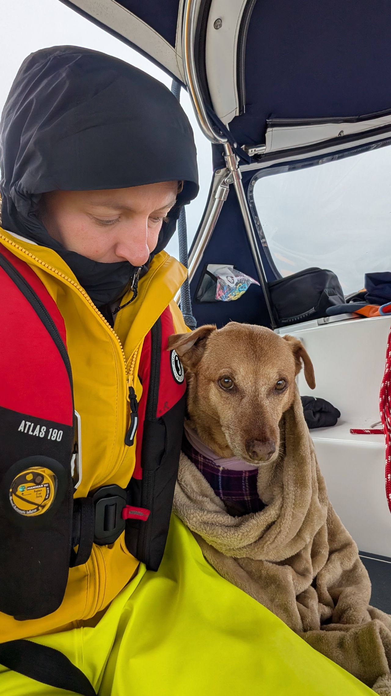 Rachel and Maui bundled up together in foul weather gear on a foggy passage day
