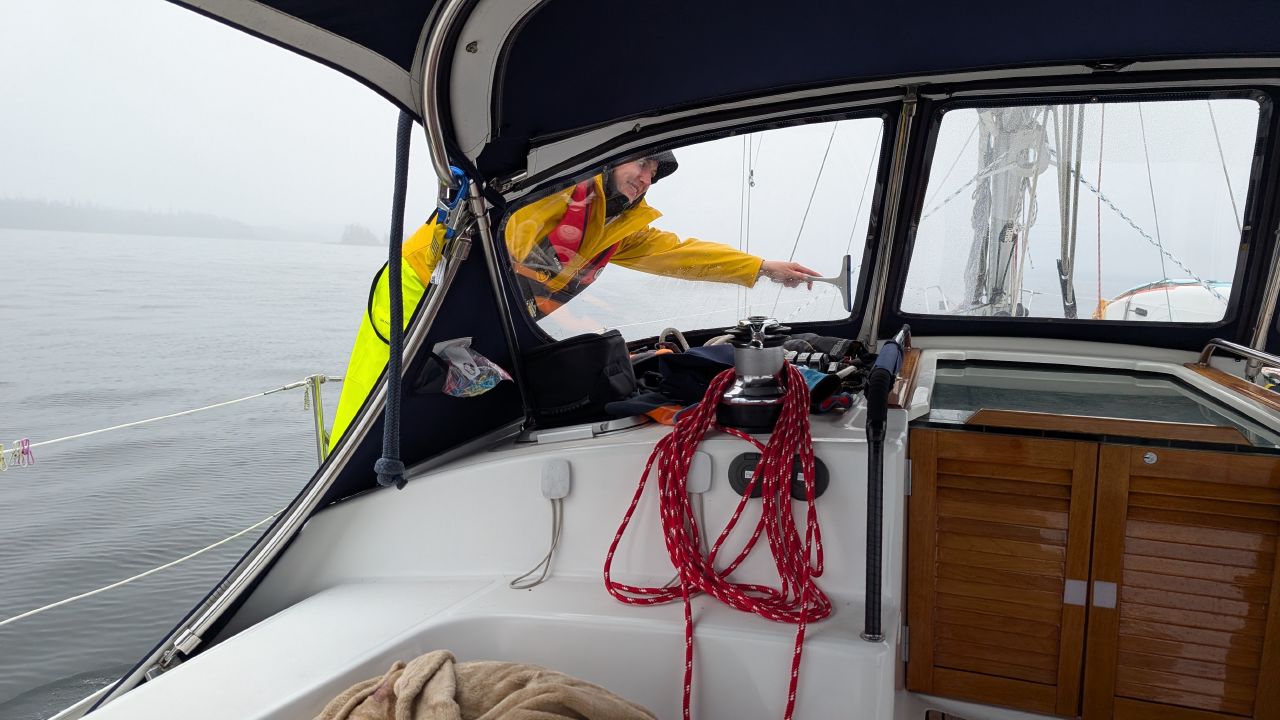 Rachel in rain gear smiling while wiping the dodger window on a foggy day