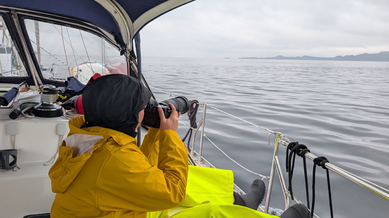 Rachel in yellow rain gear photographing whales with a camera from the deck