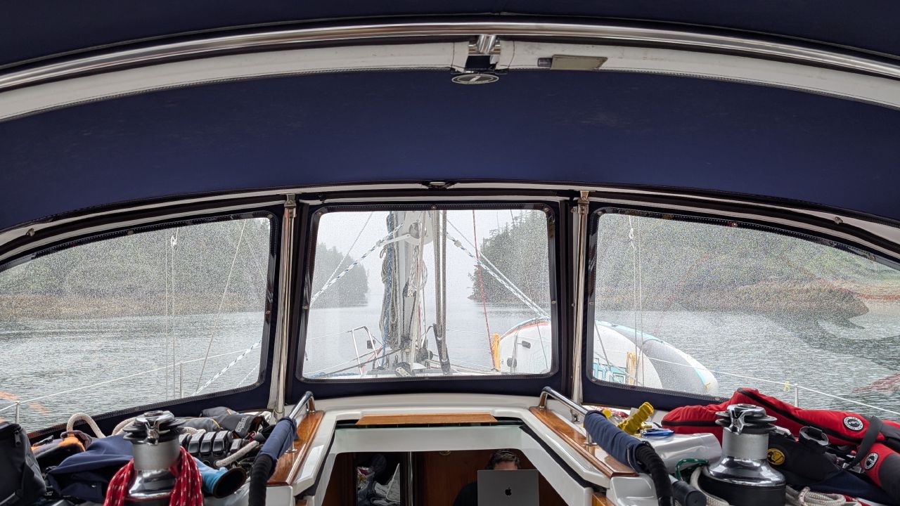 View through rain-splattered dodger windows approaching a narrow pass in the fog