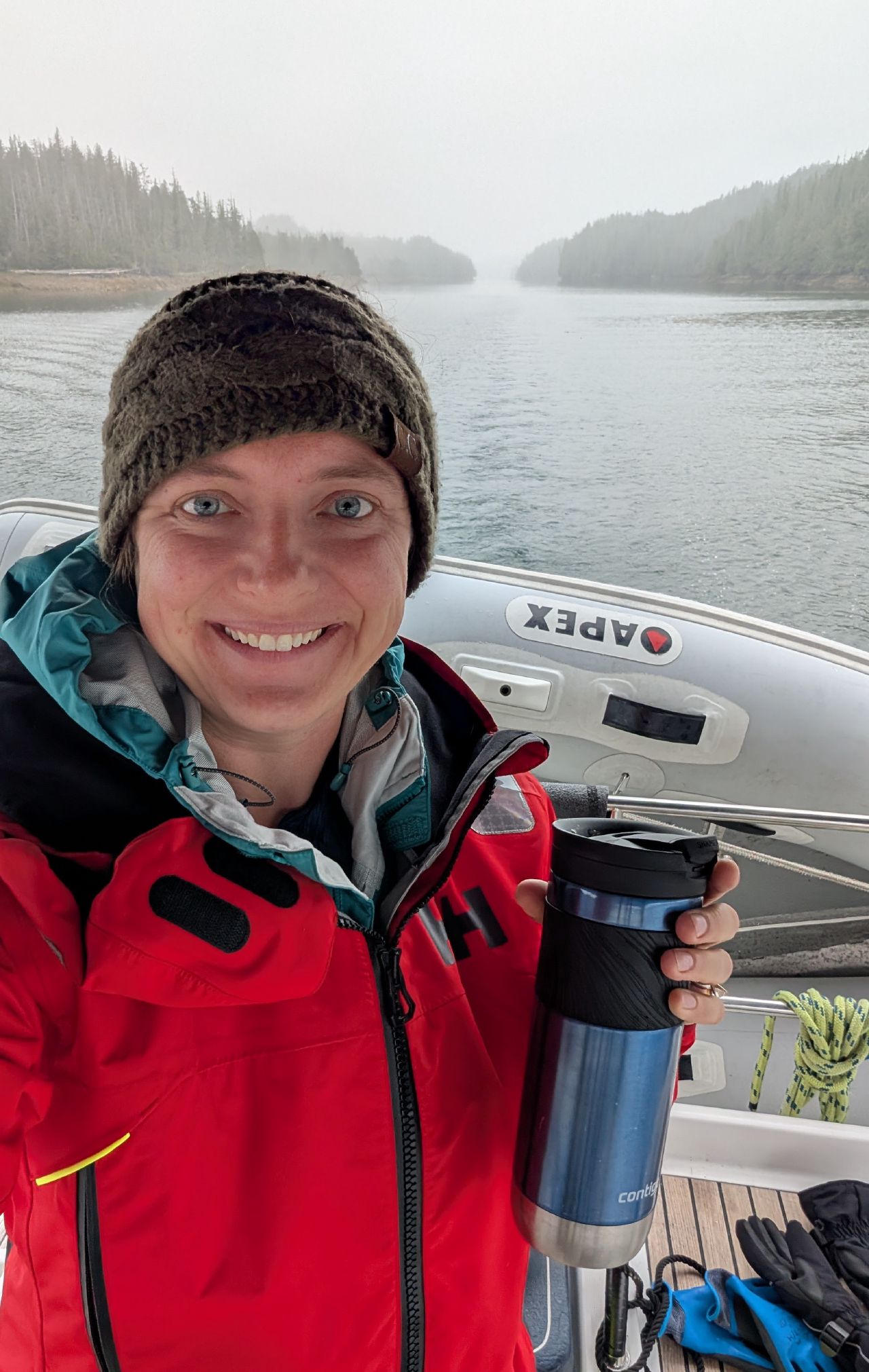 Rachel smiling selfie holding a coffee mug with the foggy Meyers Pass channel behind her