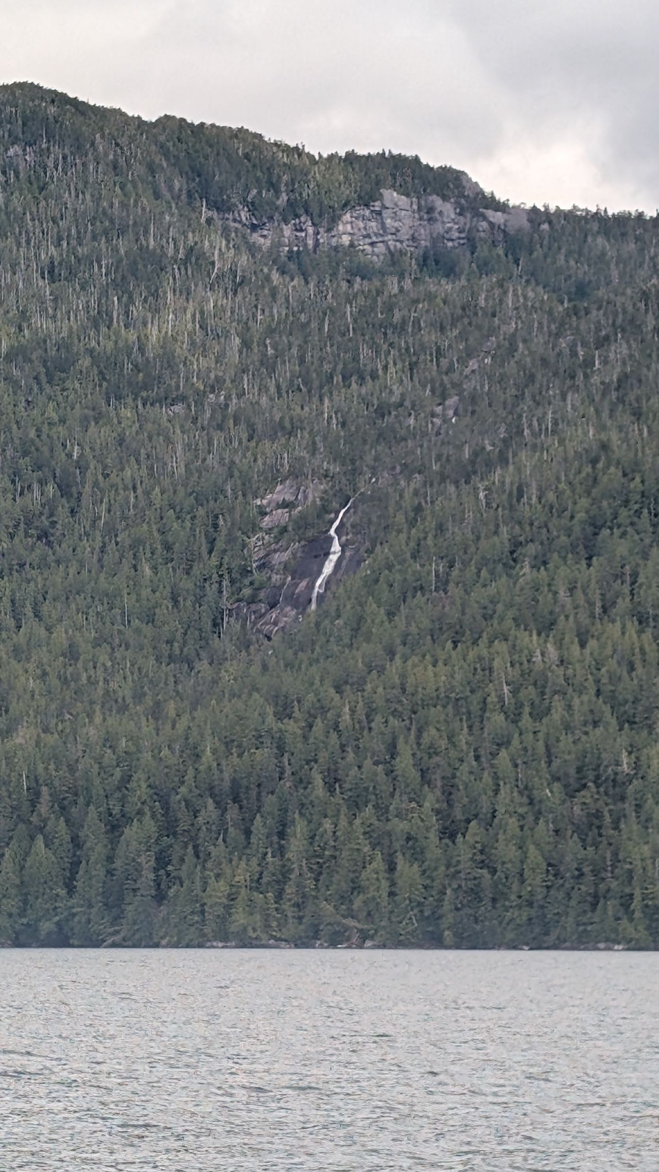 Distant waterfall cascading down a forested mountainside viewed from the water