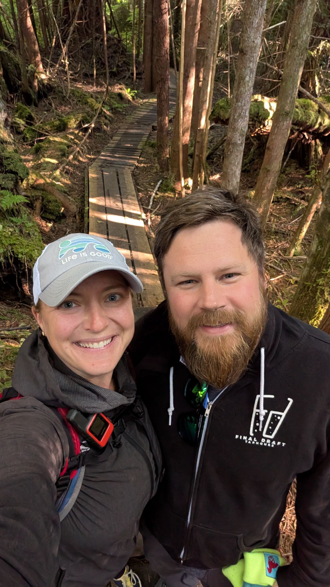 Rachel and Brian selfie on a wooden boardwalk trail through a mossy rainforest near Pruth Bay