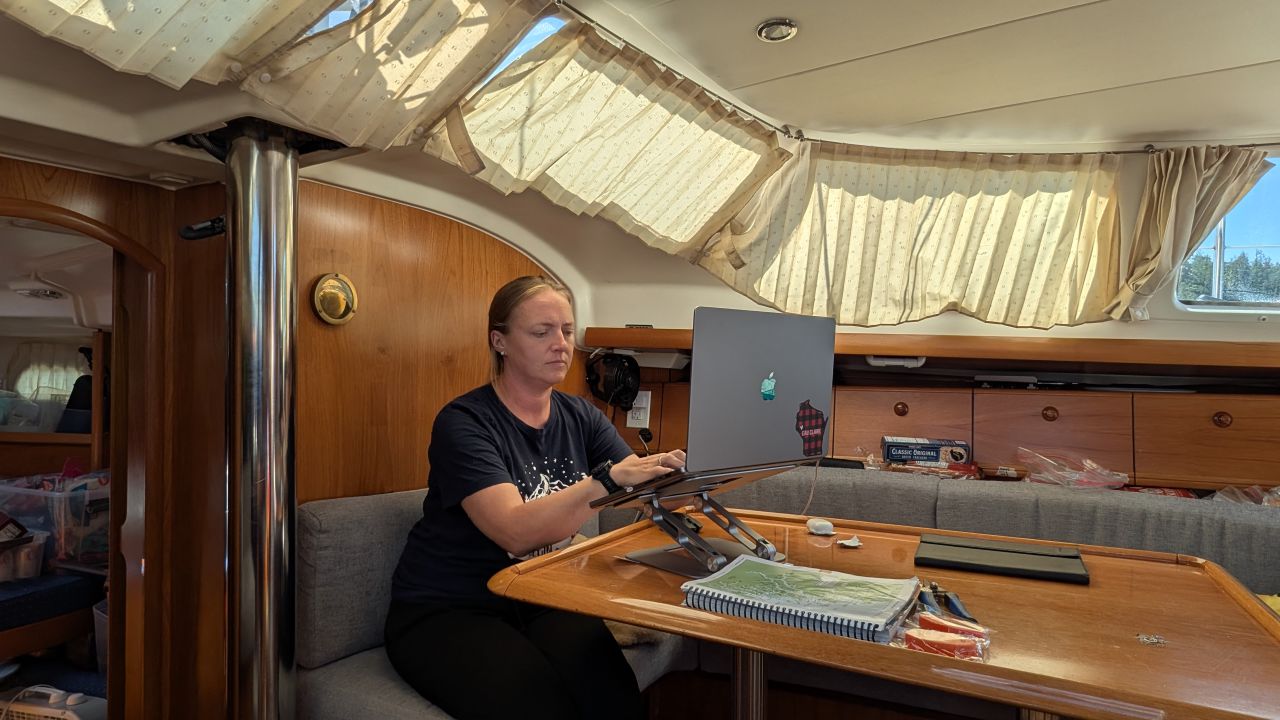 Rachel editing wedding photos on her laptop at the salon table below deck on SV Yahara