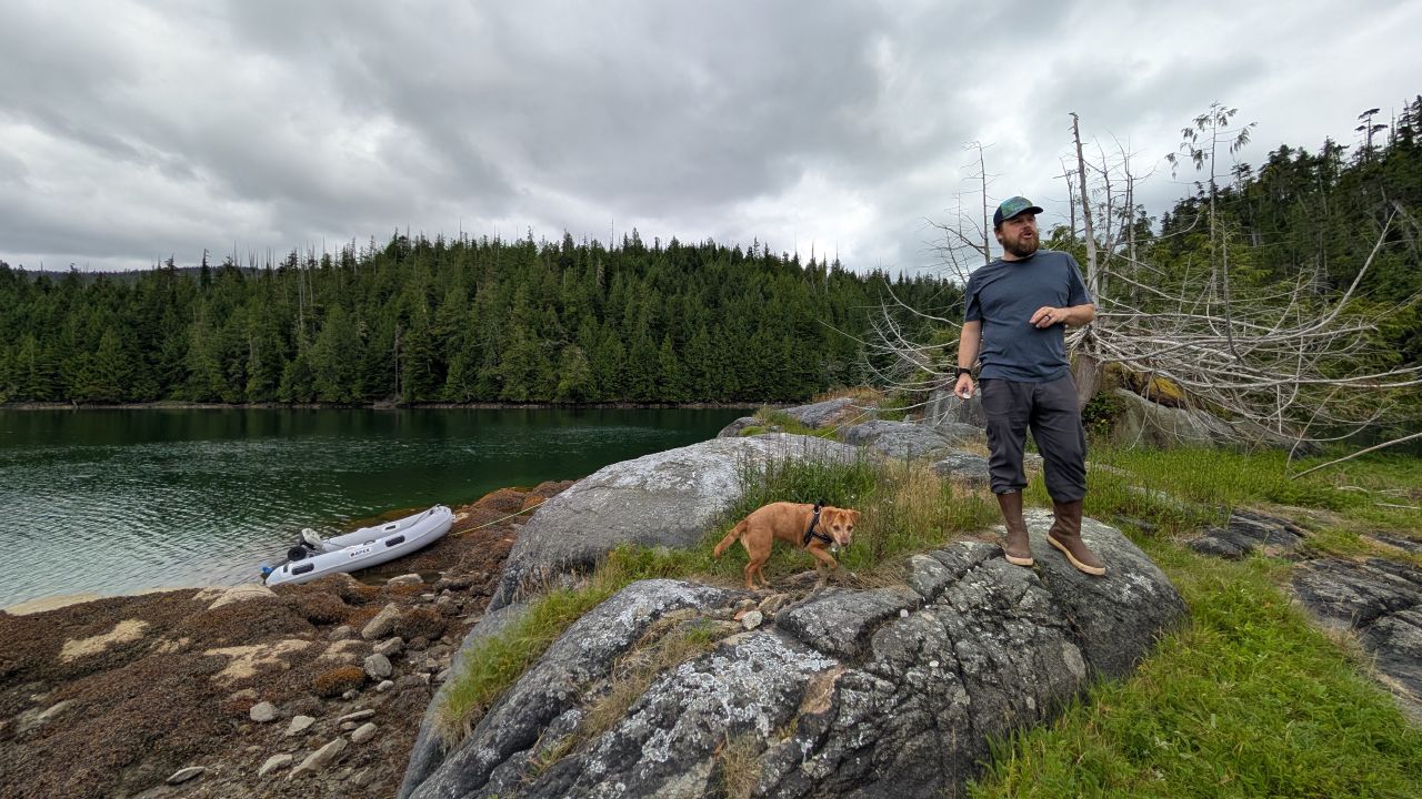 Brian and Maui standing on the rocky shore at Berry Cove with the dinghy pulled up and green water below