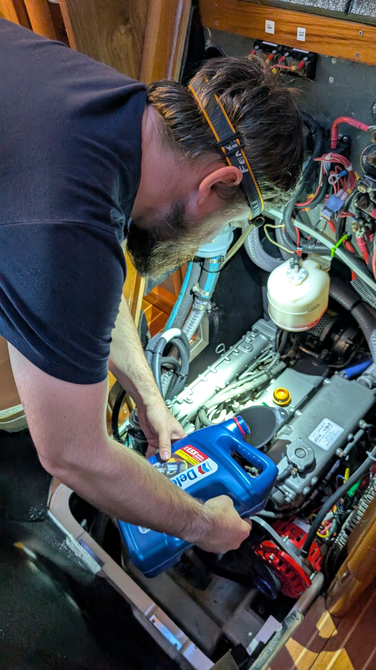 Brian doing a partial engine oil change in the engine compartment of SV Yahara wearing a headlamp