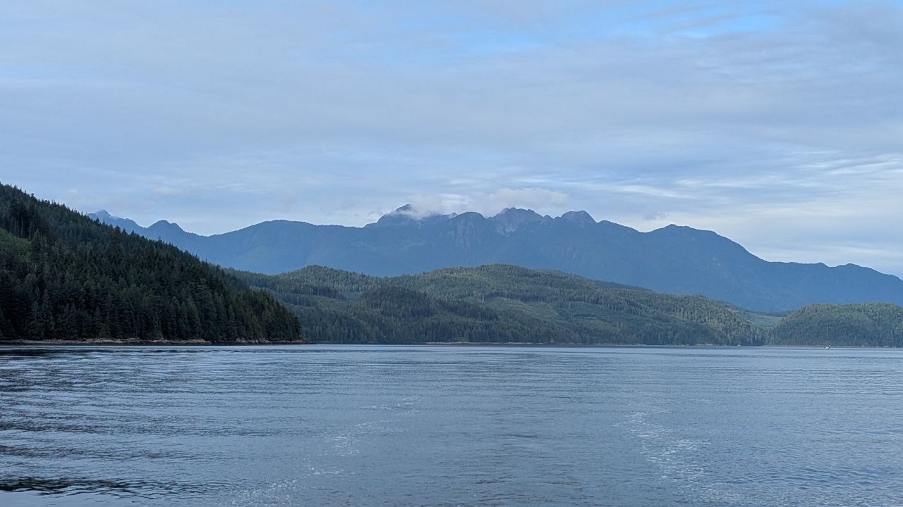 Layered mountains and forested coastline near Green Point Rapids with clouds hovering over the peaks