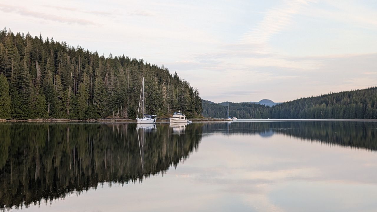 Sailboat and powerboat anchored in the calm, mirror-like waters of Hanfeld Bay surrounded by evergreen forest
