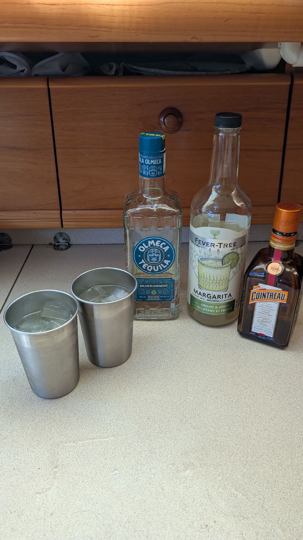 Margarita supplies lined up on the galley counter: tequila, Fever-Tree mix, Cointreau, and stainless steel cups