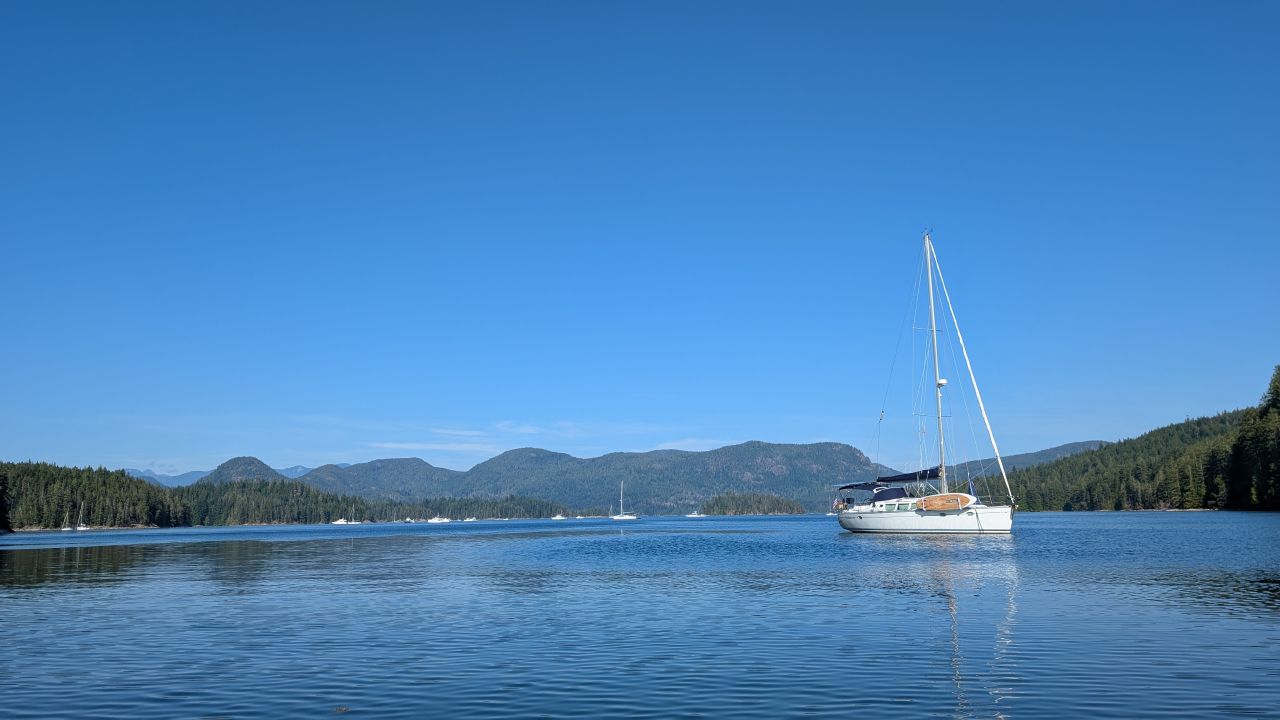 SV Yahara at anchor under a clear blue sky at Octopus Islands with forested mountains behind