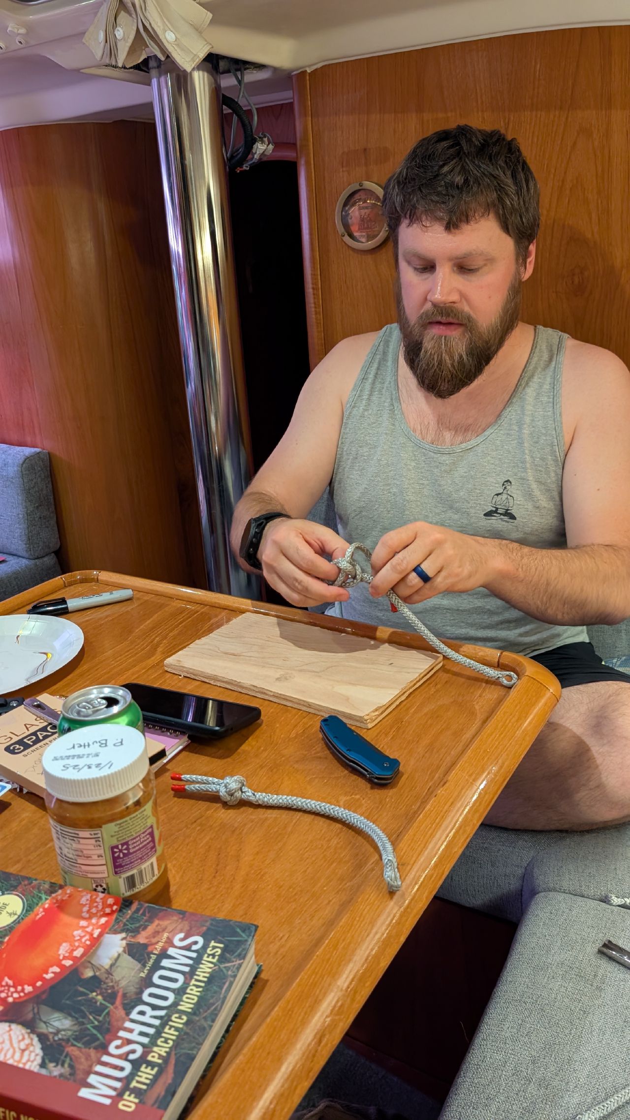 Brian making soft shackles from Dyneema line at the saloon table with a mushroom field guide nearby