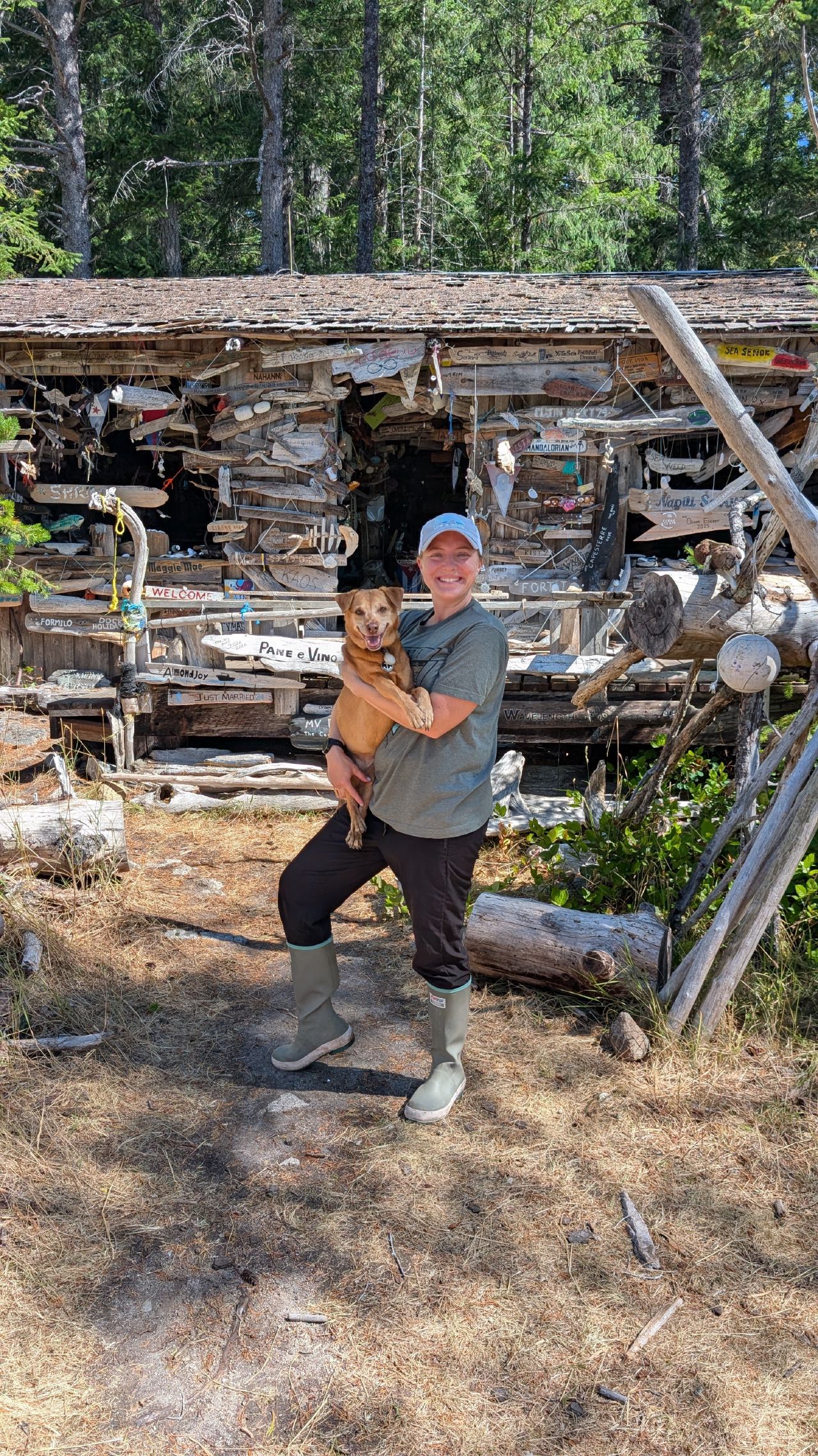 Rachel holding Maui in front of the driftwood cabin decorated with boat names and art at Octopus Islands