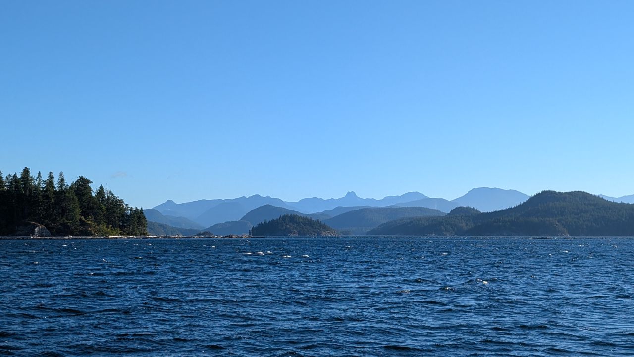 Windy blue water with whitecaps and layered mountain silhouettes approaching Heriot Bay