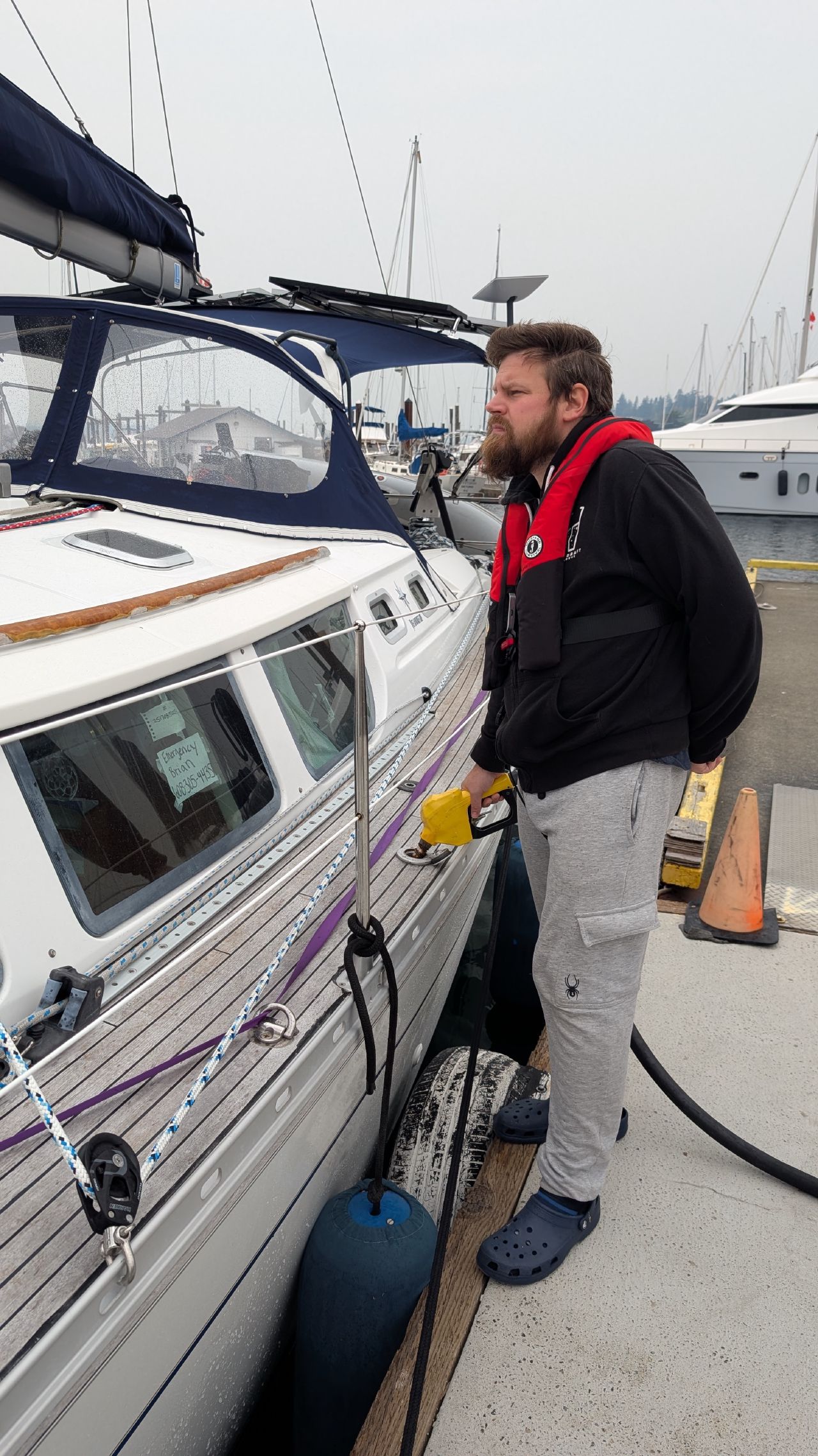 Brian in a life jacket fueling up SV Yahara at the Comox Valley Marina fuel dock on a smoky overcast day