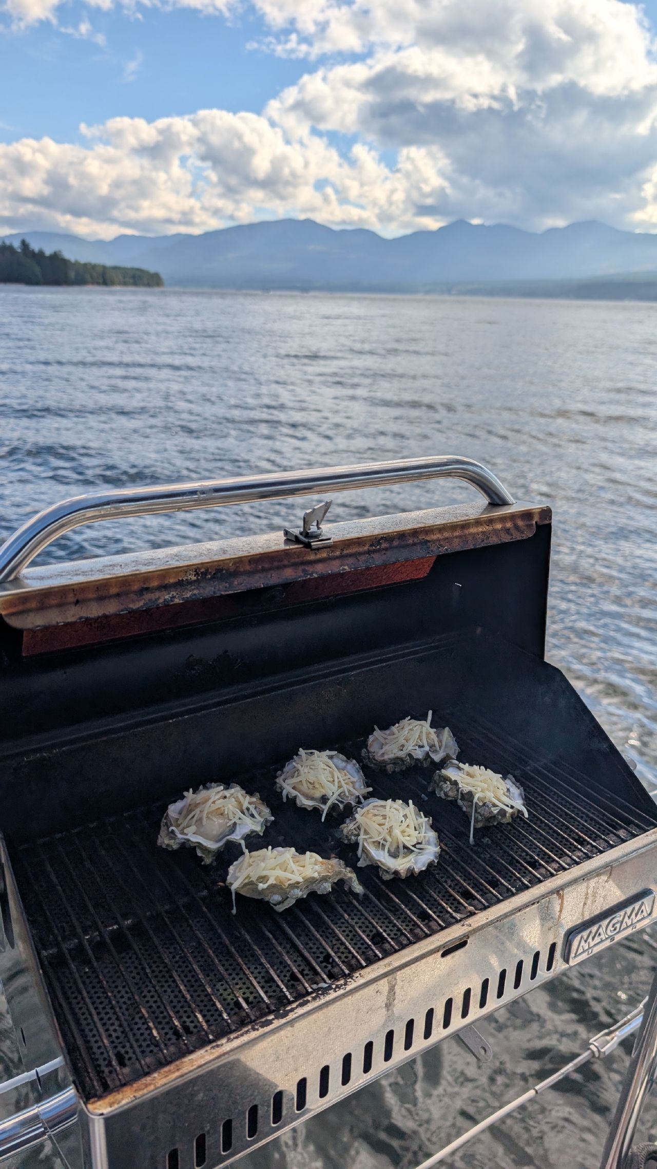 Oysters Rockefeller topped with cheese grilling on the Magma BBQ with mountains and water in the background