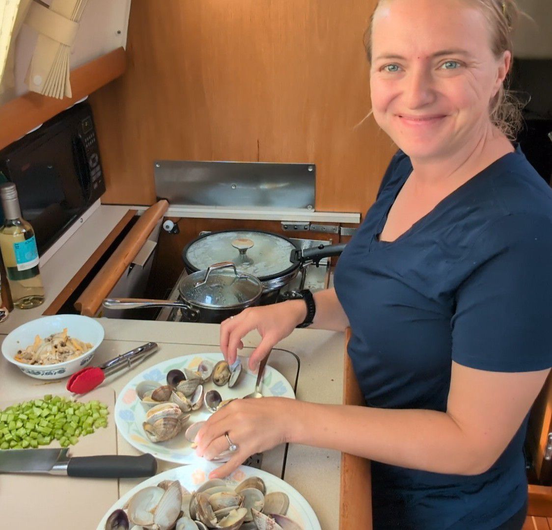 Rachel smiling while shucking freshly steamed clams in the galley with chopped celery ready on the counter