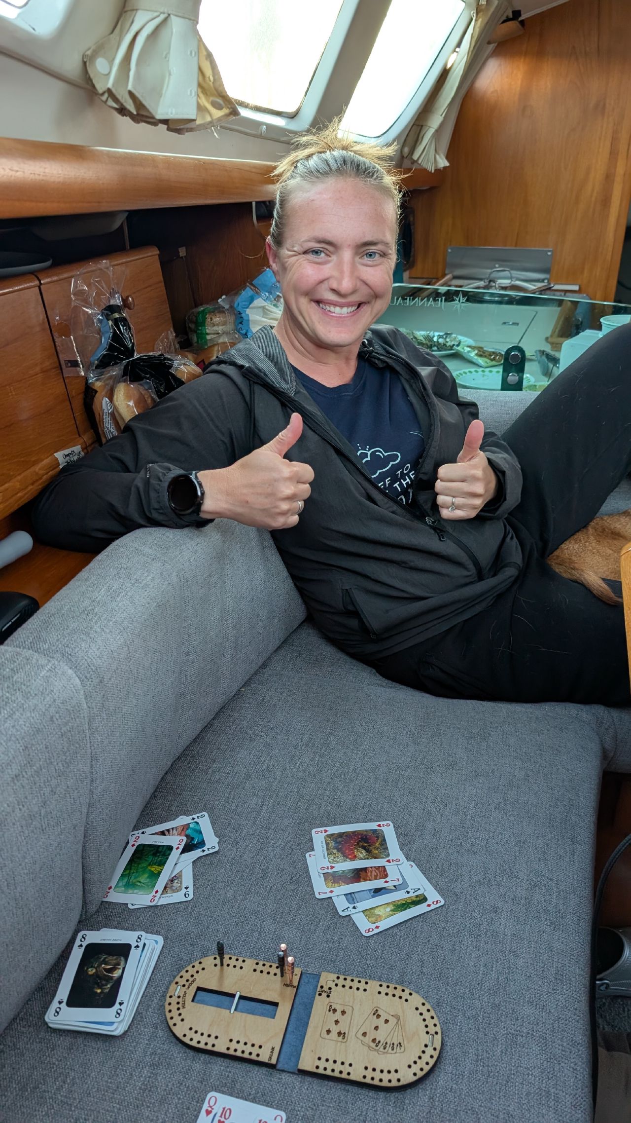 Rachel giving two thumbs up after winning at cribbage on the mini board below deck