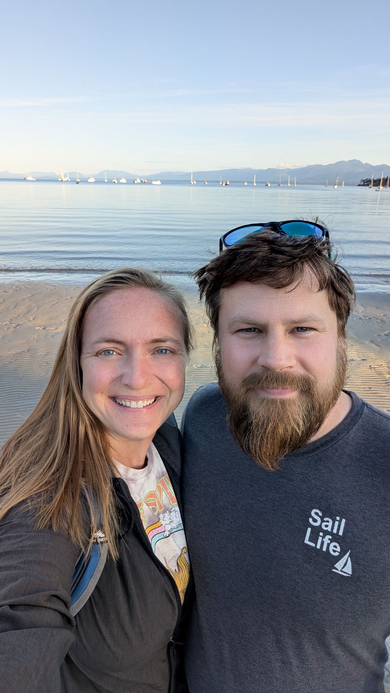 Rachel and Brian selfie on the sandy beach at Tribune Bay with anchored boats in the background
