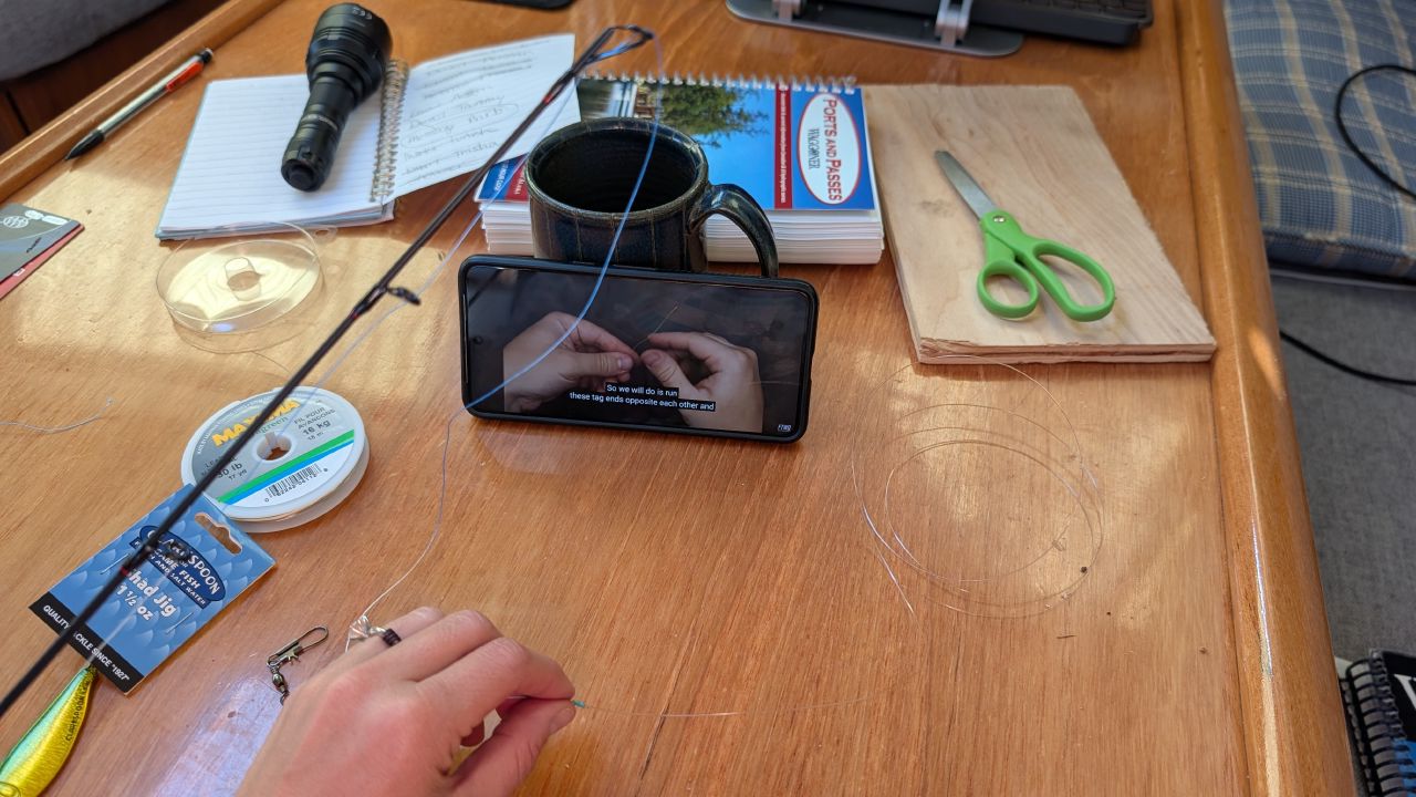 Tying a fishing leader line on the boat’s cabin table while watching a tutorial video on a phone