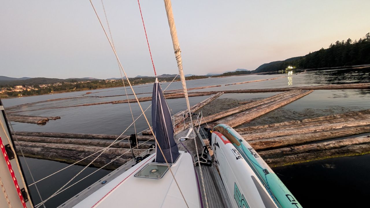 View from the bow of SV Yahara surrounded by logs from a drifting log boom in Ladysmith anchorage at dawn